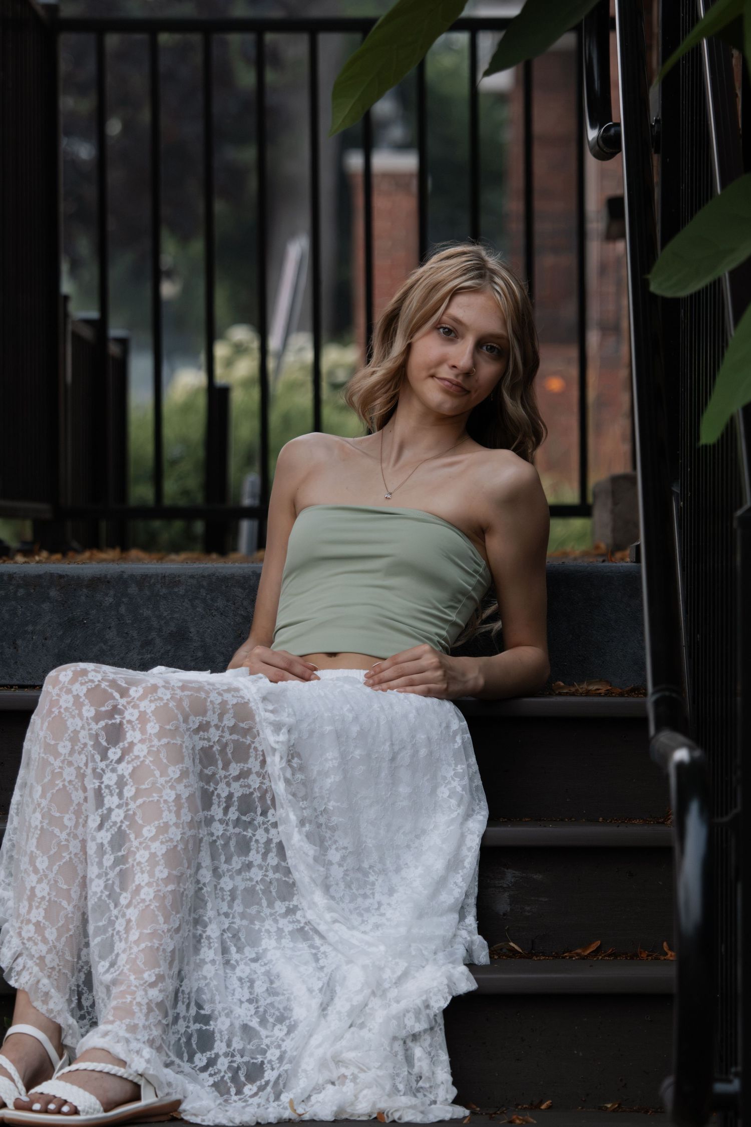 Young blonde woman in sage green tube top and white lace skirt sitting on steps.