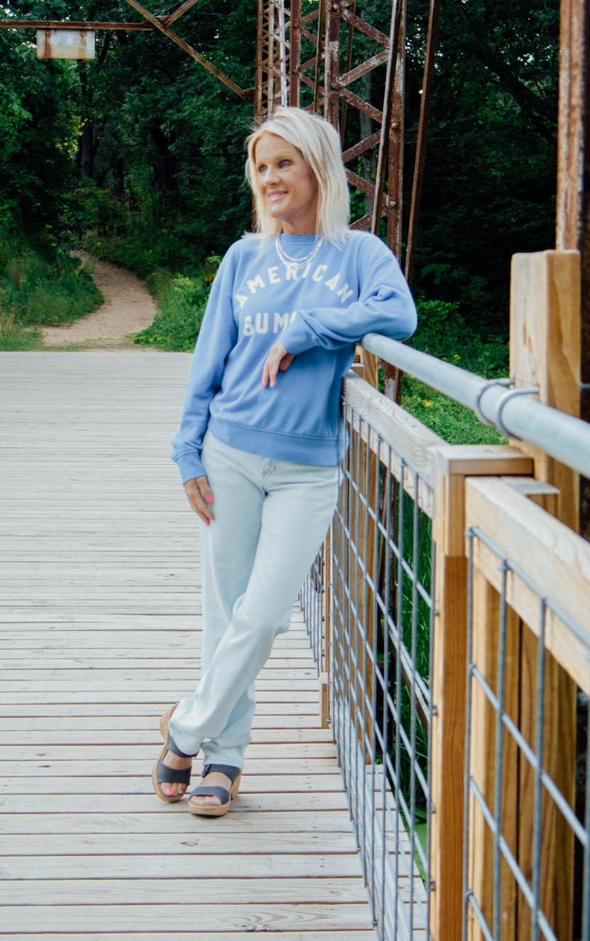 Person in casual blue loungewear strikes playful poses on a wooden boardwalk surrounded by nature.