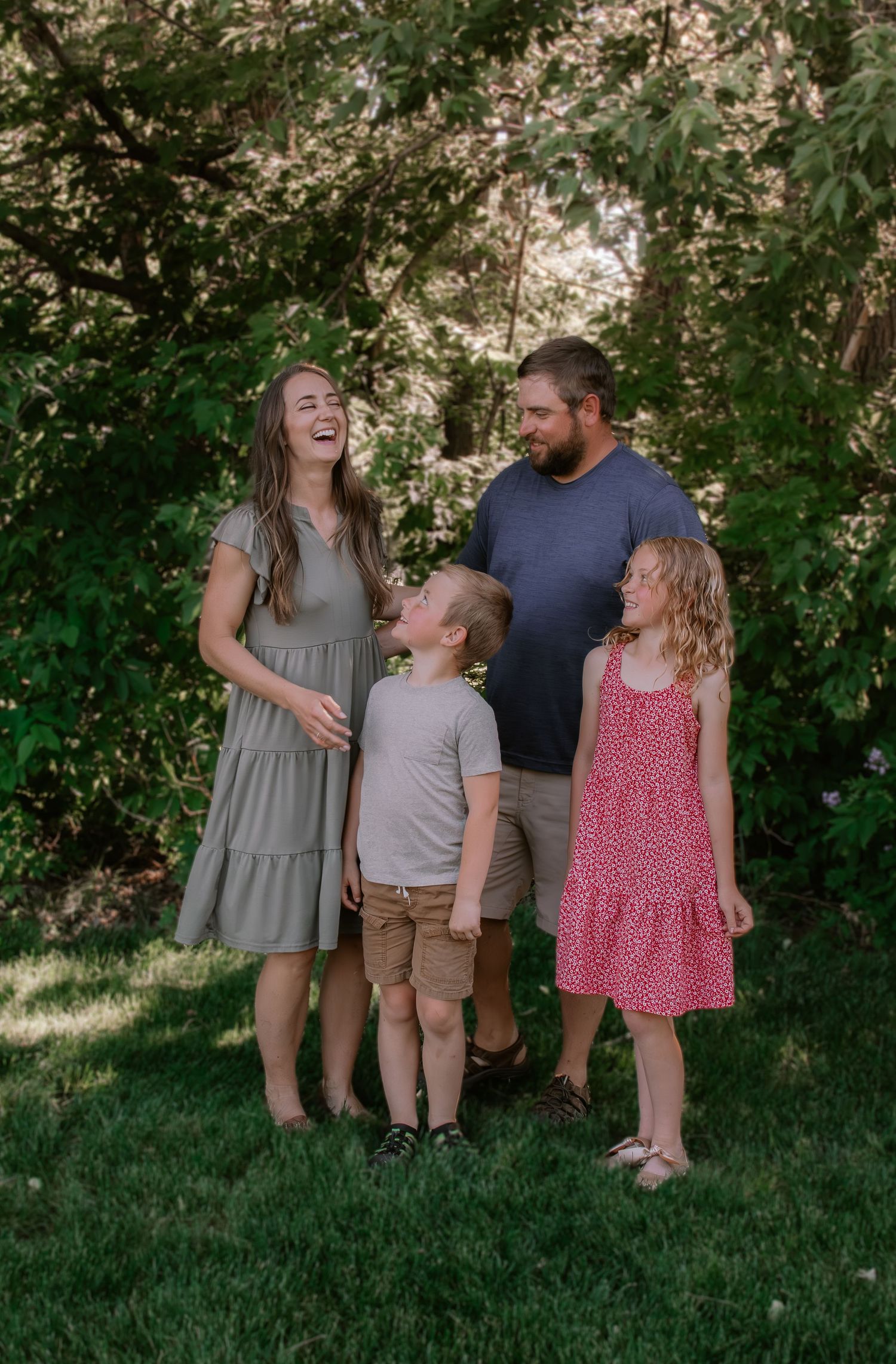 Happy family of four laughing together outdoors in a lush green garden setting.