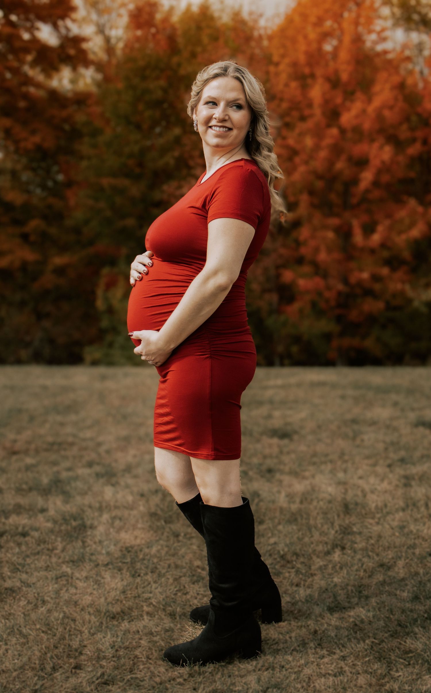 Maternity photos taken in a field with beautiful fall colors in the background.