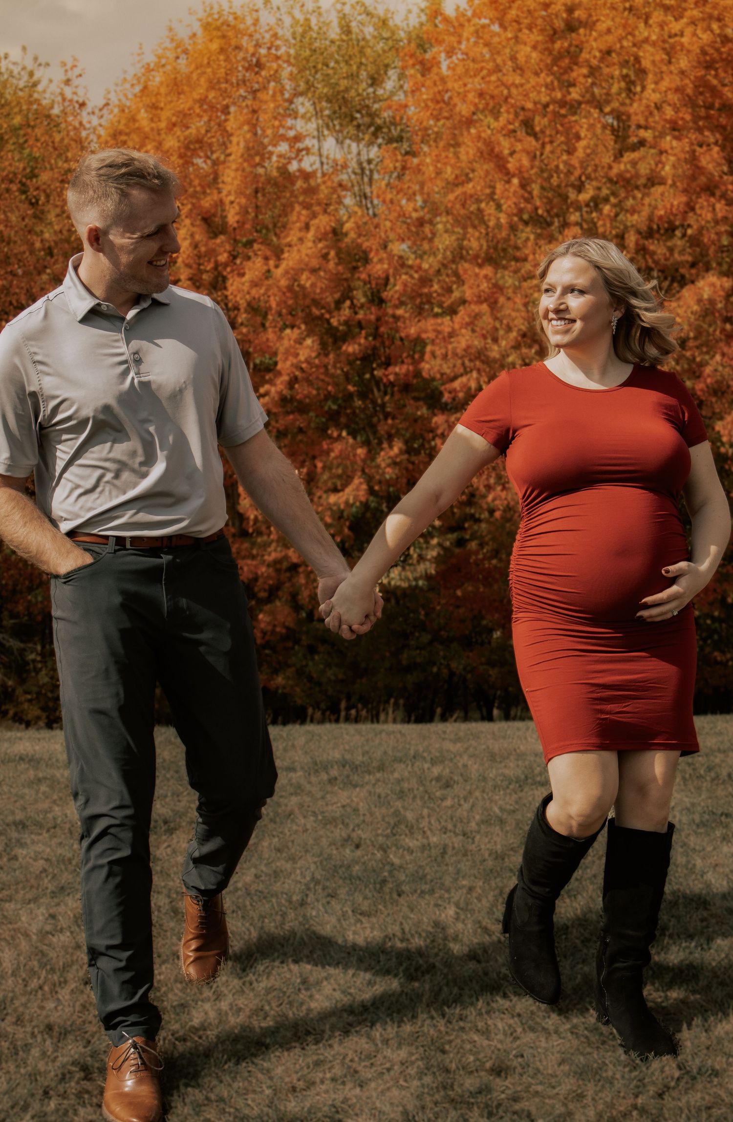 Couple in red and gray outfits posing against vibrant orange fall foliage backdrop.