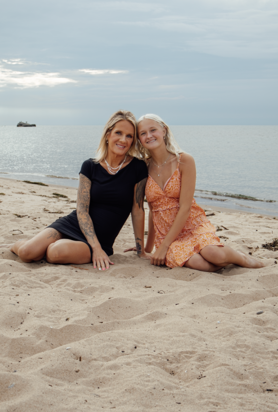 Two people relaxing together on a sandy beach during sunset with cloudy skies overhead.