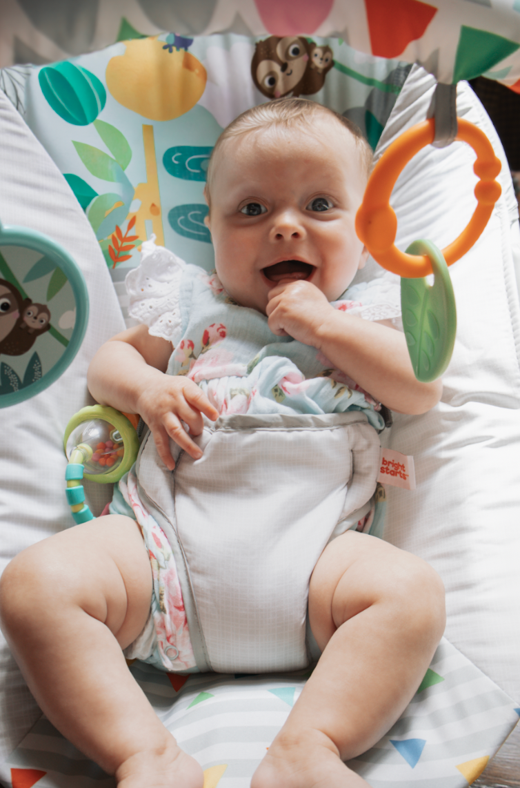 A small baby wearing white lying on patterned bedding with colorful decorative elements visible above.