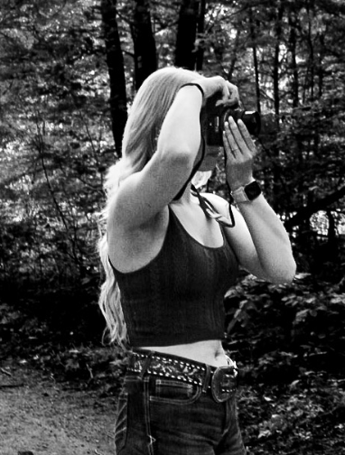 A photographer in black clothes takes photos in a wooded setting during a photoshoot.