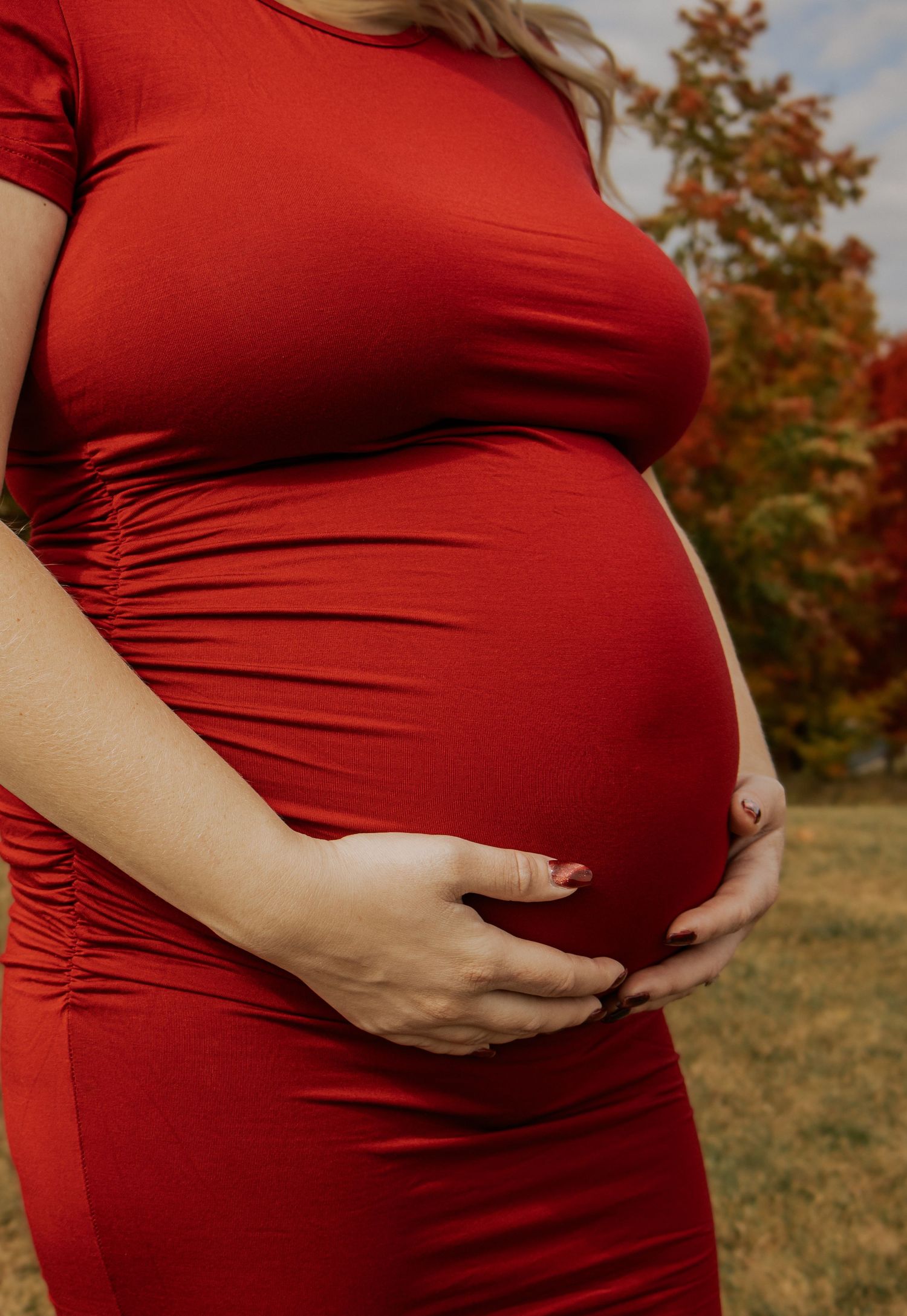 Close-up shots of pregnant belly in red dress with hands cradling the bump.