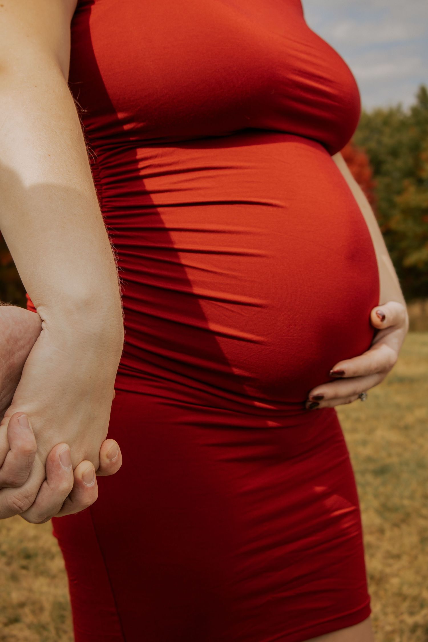Close-up shots of a pregnant belly in a red dress against an autumn backdrop.