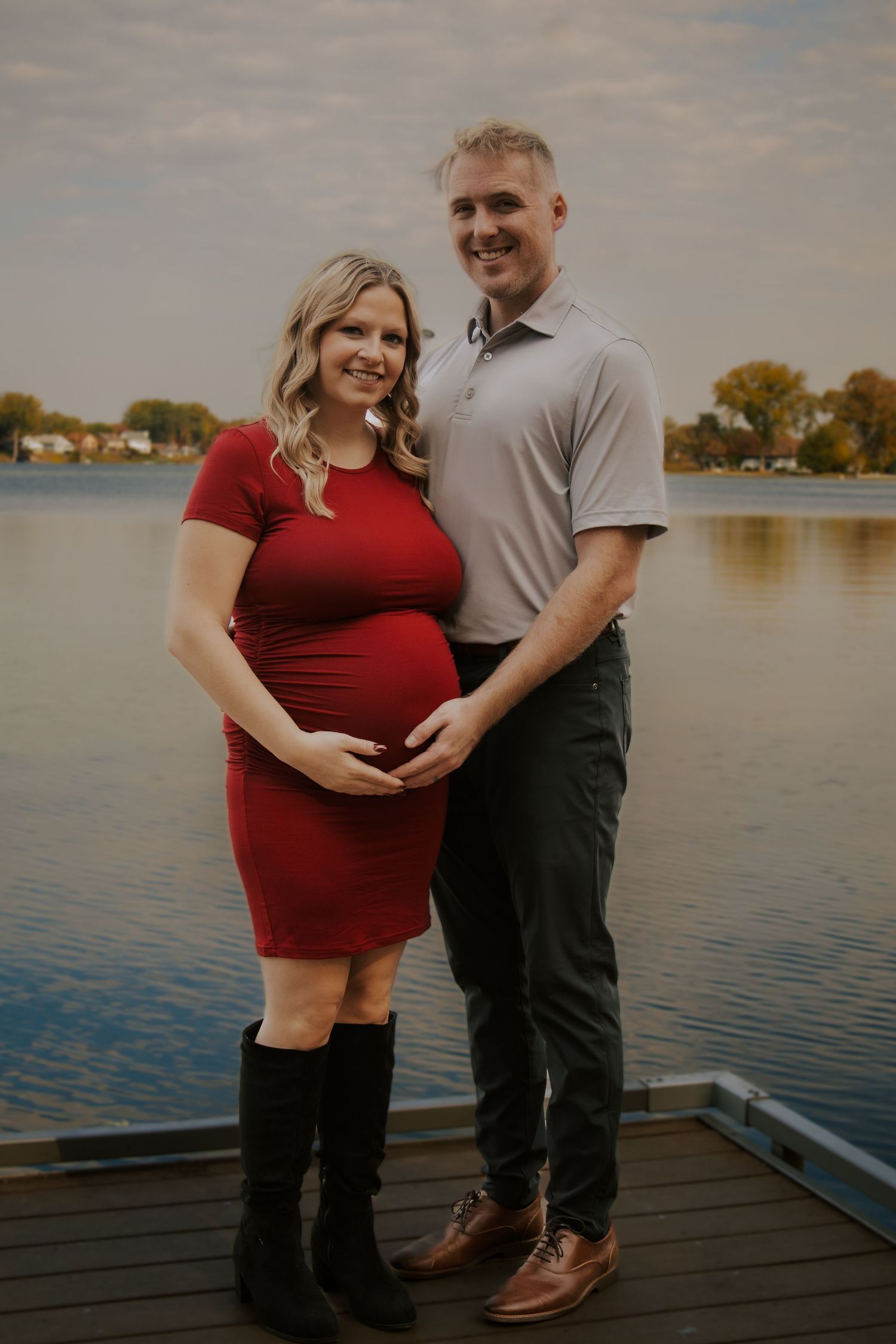 Maternity photos taken on a wooden dock by a serene lake during sunset.