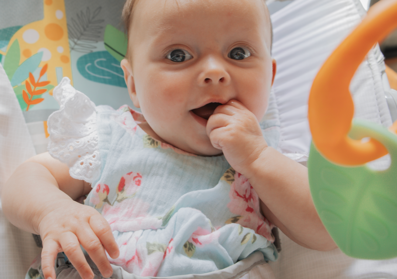 Close-up shot of baby lying on white bedding with orange and green decorative elements visible.