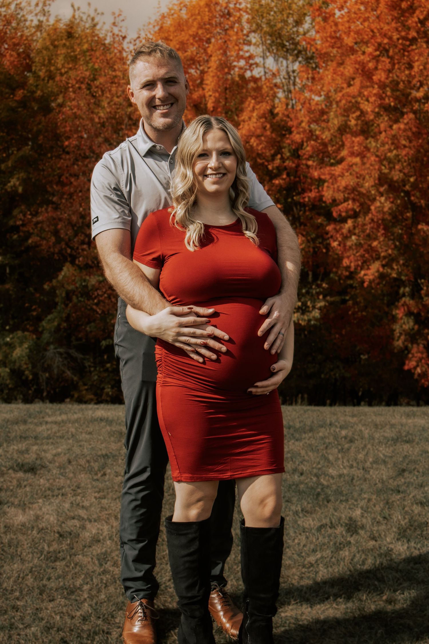 A couple poses together in front of vibrant autumn foliage wearing red and grey outfits.