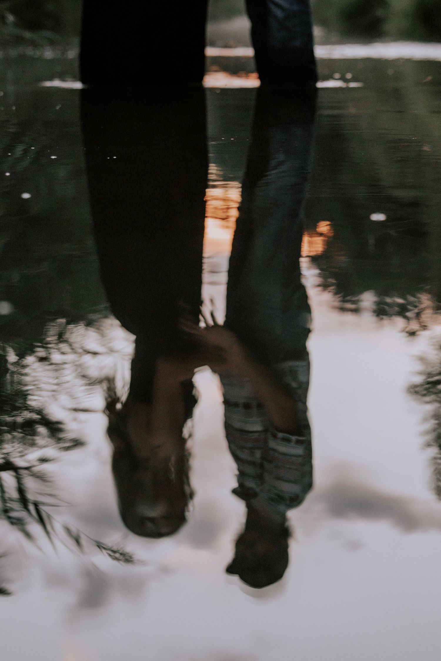 Reflection of two people standing together mirrored in a rain puddle on a dark wet surface.
