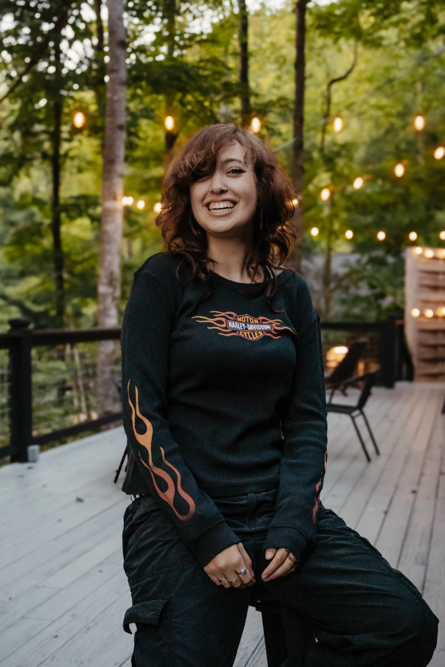 Person wearing black sweatshirt with flame design sits on wooden deck with string lights in background.