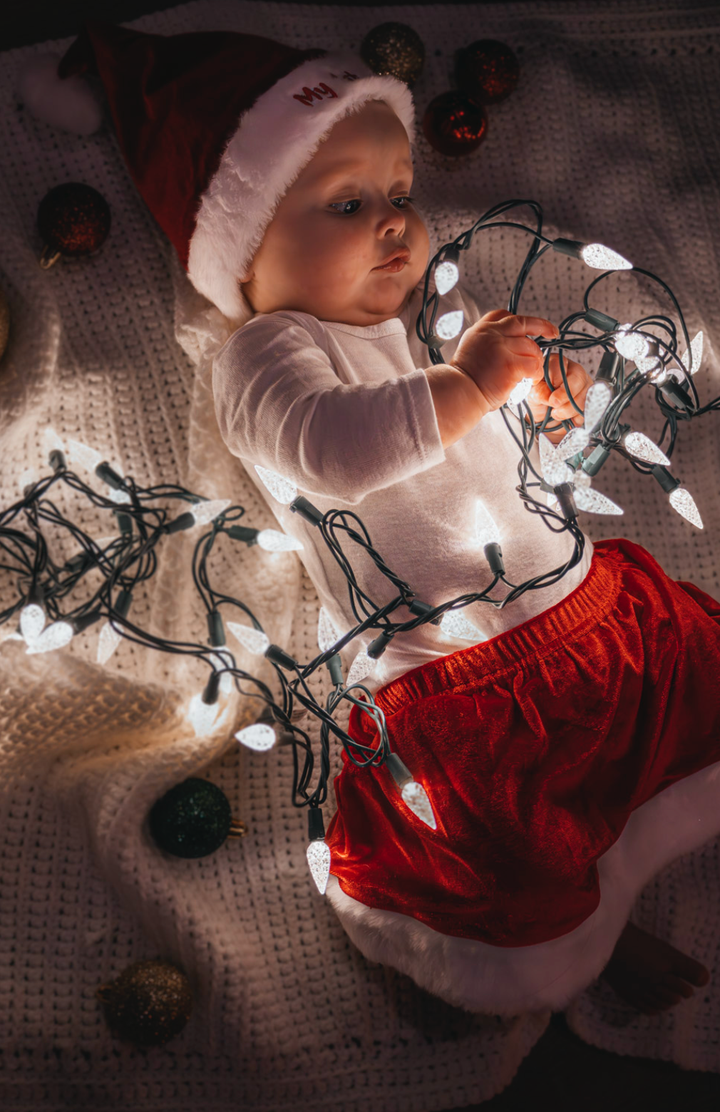 White Christmas lights illuminate a cozy scene with red stockings and knitted textures in warm lighting.