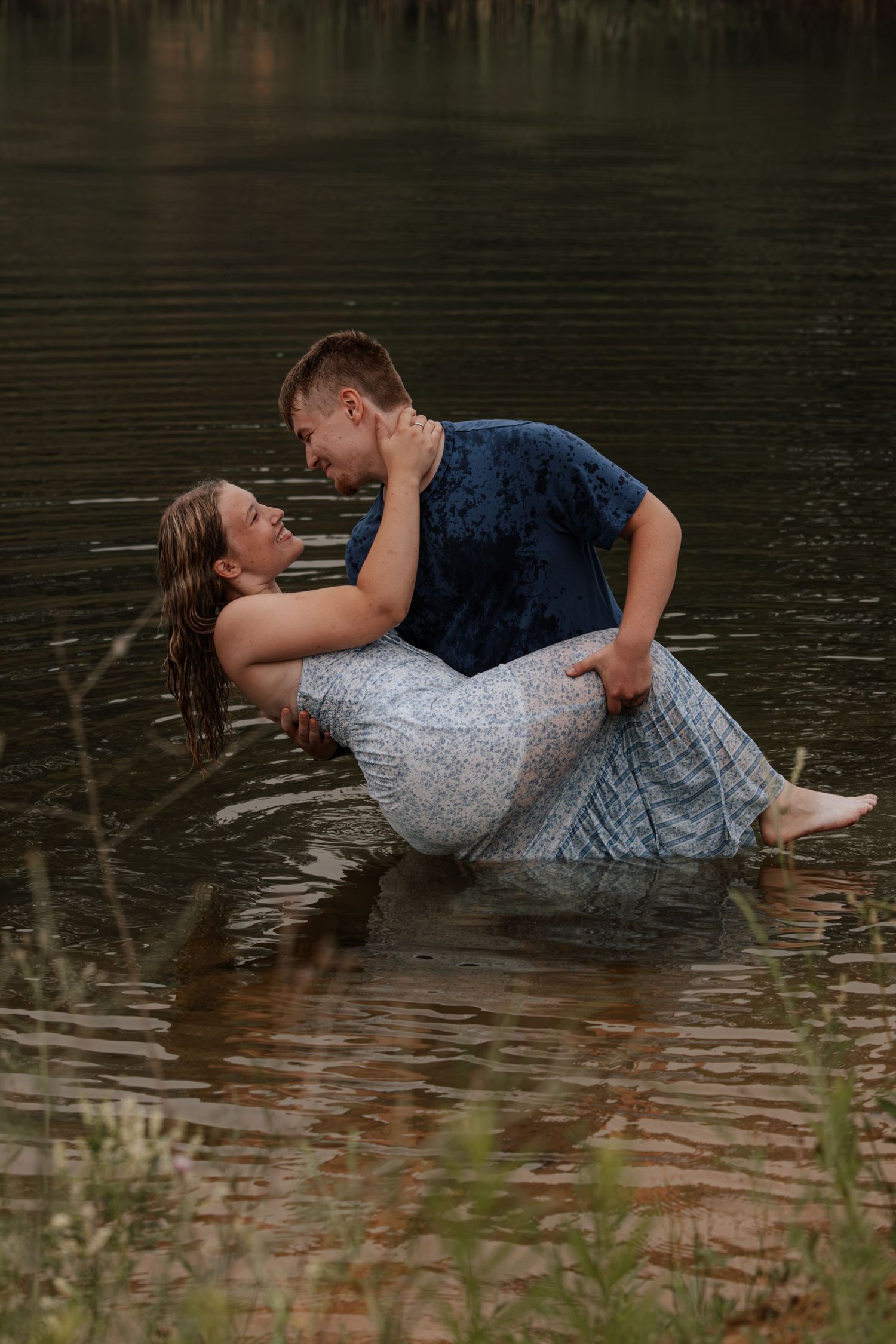 Couple sharing a romantic dance in a lake, woman in floral dress dipped back by man in blue shirt.