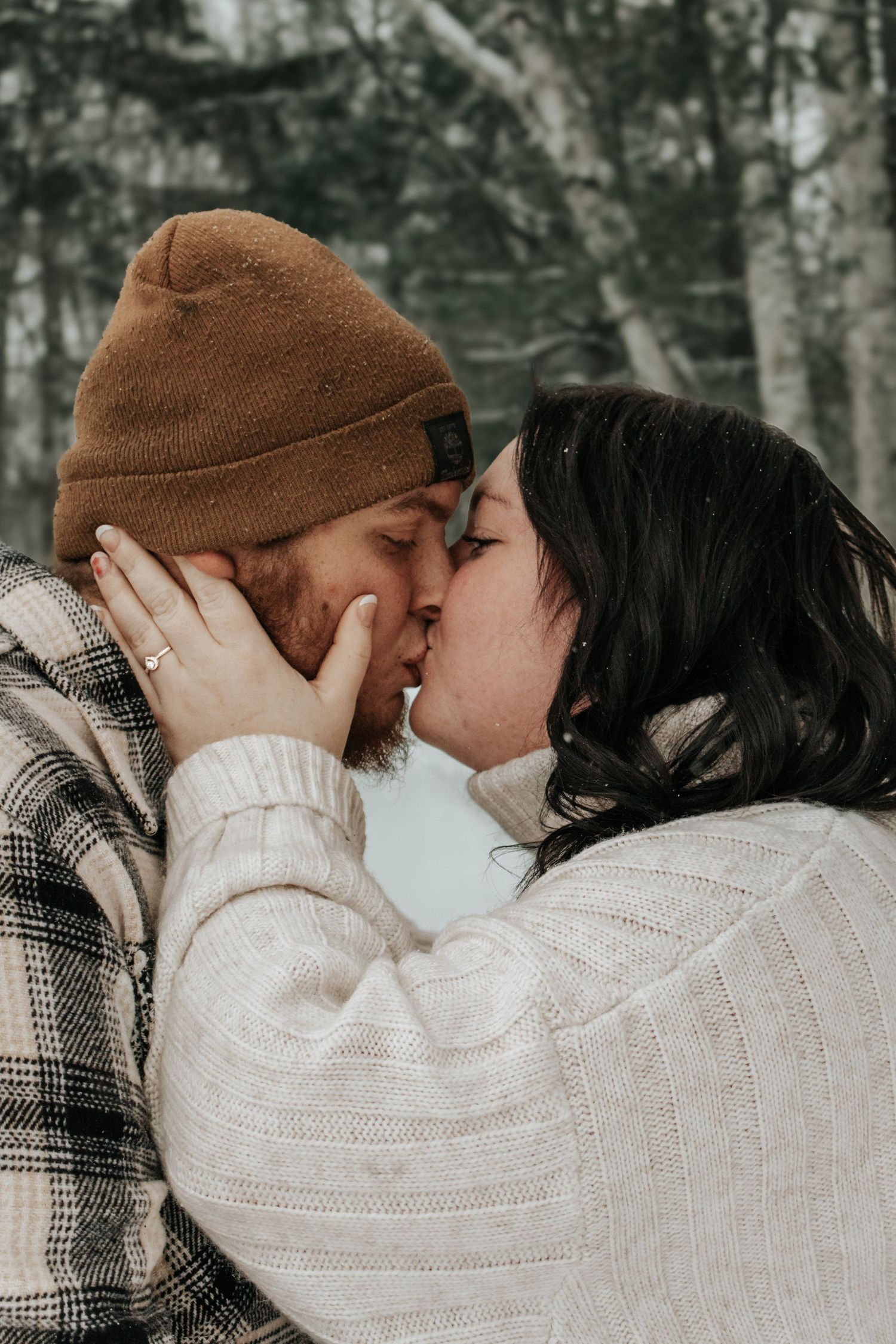 A romantic winter moment captured between a couple in cozy sweaters kissing outdoors among birch trees.