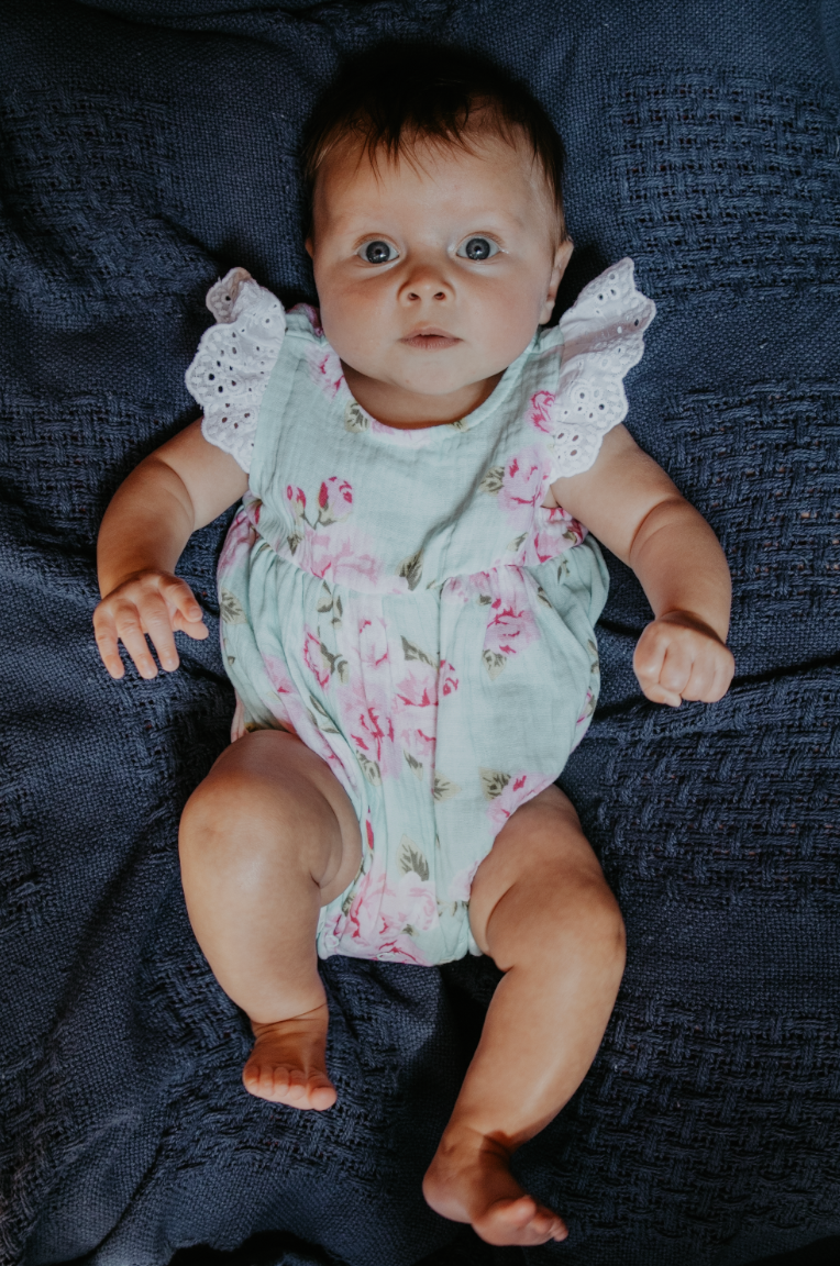 Baby in white floral romper lying on dark blue textured fabric displaying various expressions.
