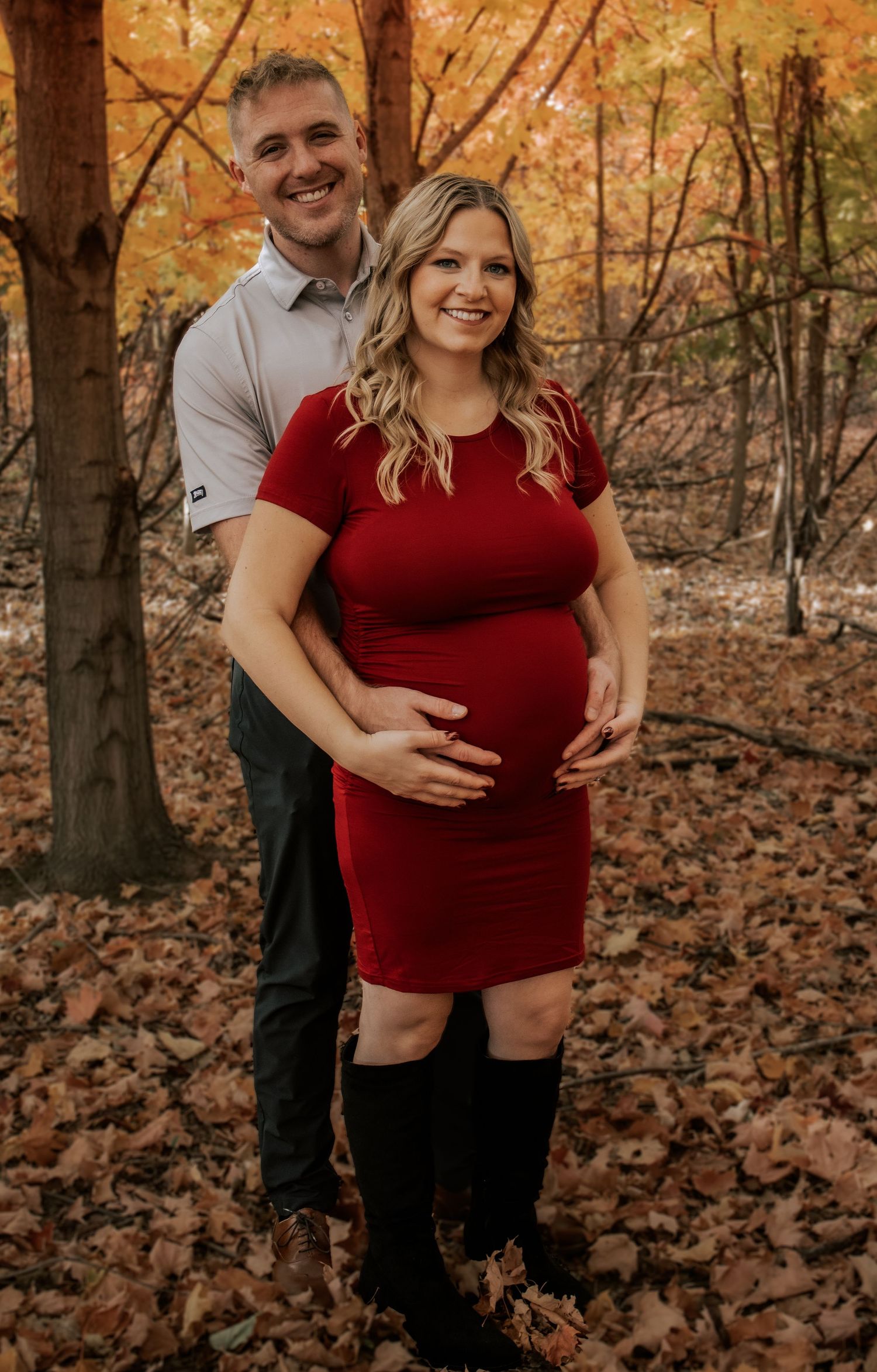 Maternity photoshoot in a wooded area with red and orange autumn leaves.