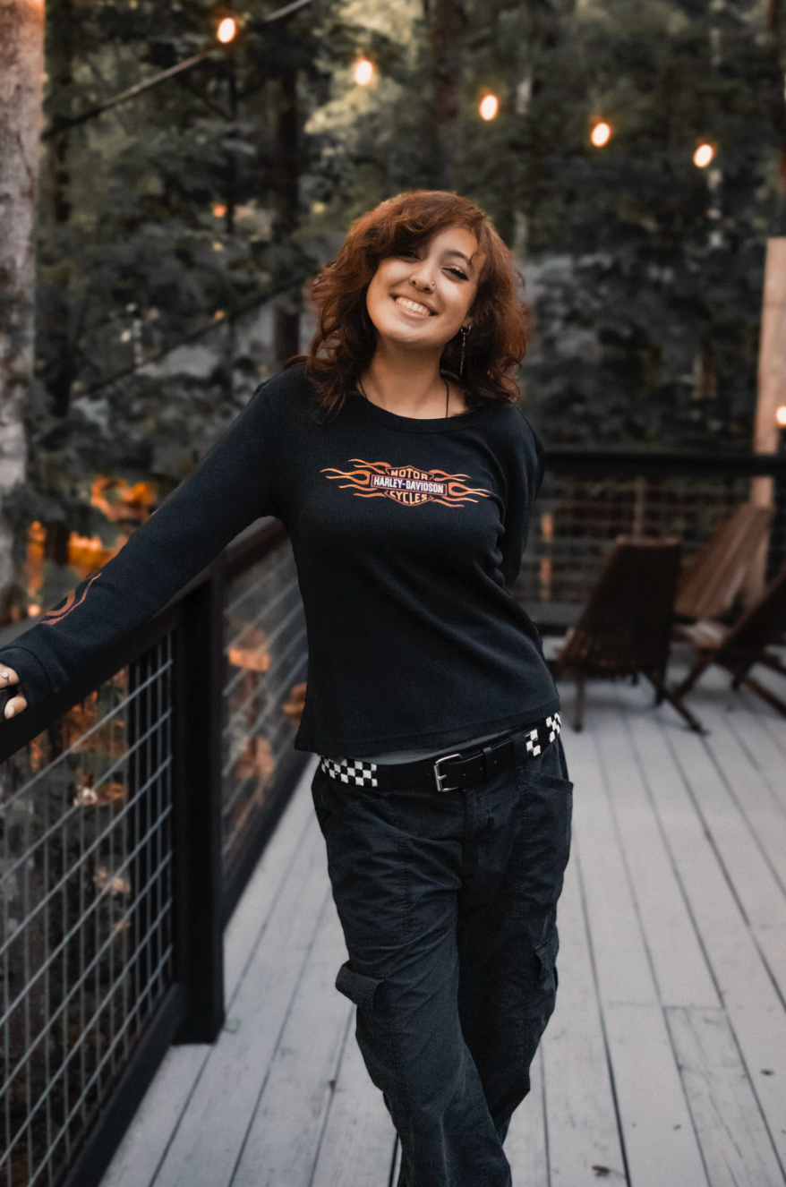 Person in black clothing dances joyfully on wooden deck with string lights overhead in outdoor evening setting.