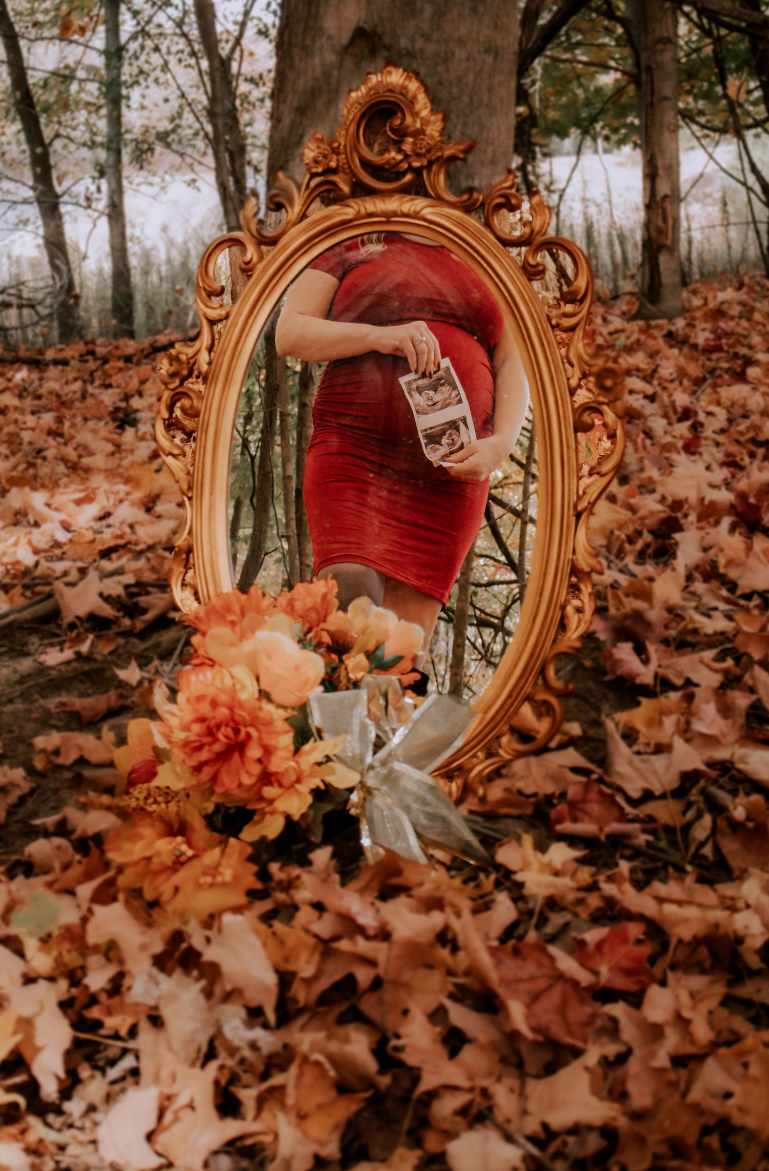 Ornate gold vintage mirror surrounded by autumn leaves and orange flowers in a forest setting.