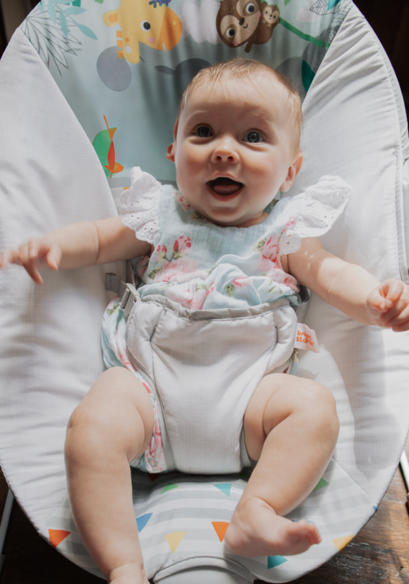 A baby in white clothing smiling while lying on decorated nursery bedding with playful animal designs.