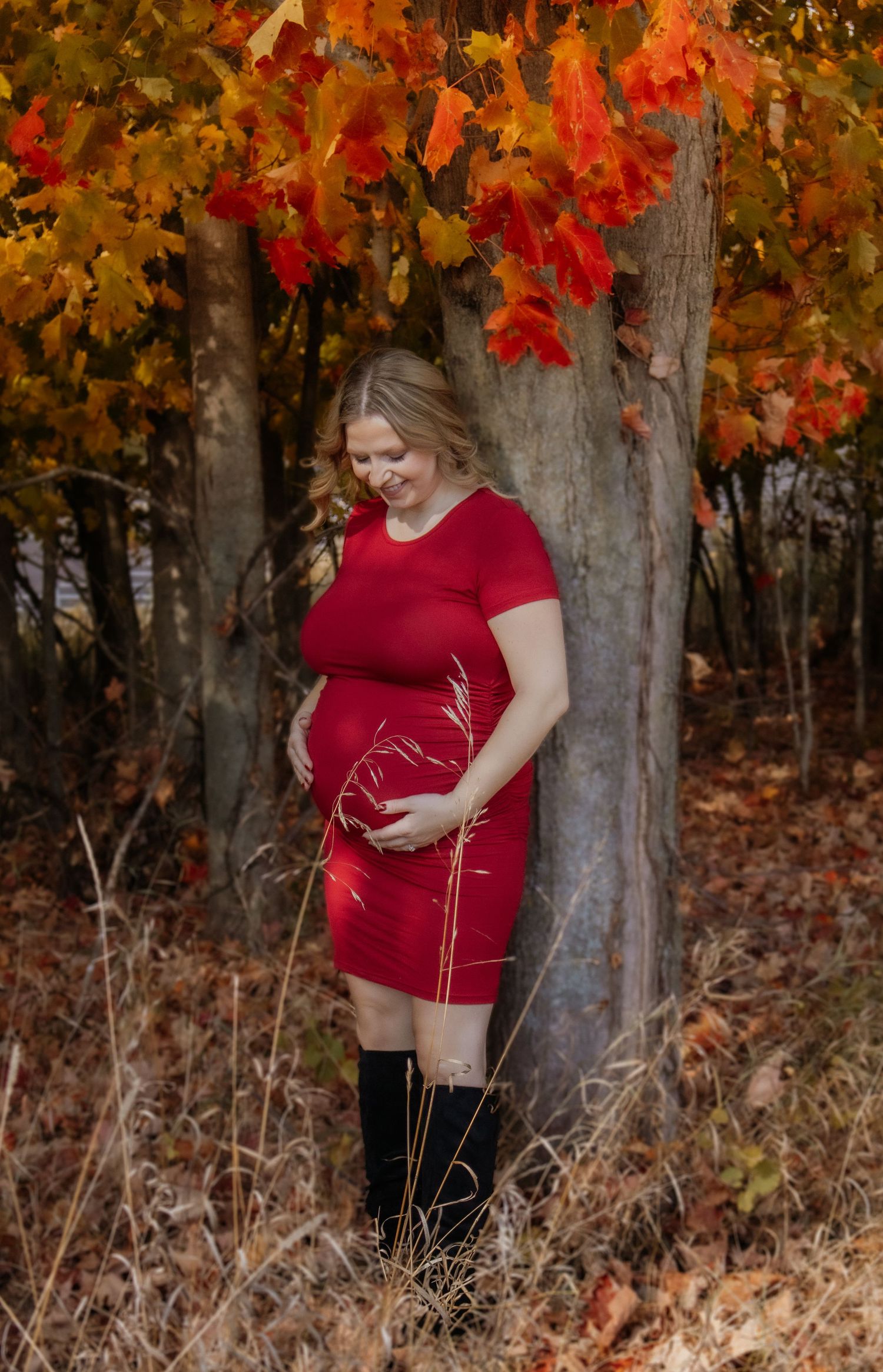 Maternity portrait against autumn trees with vibrant red and orange leaves.