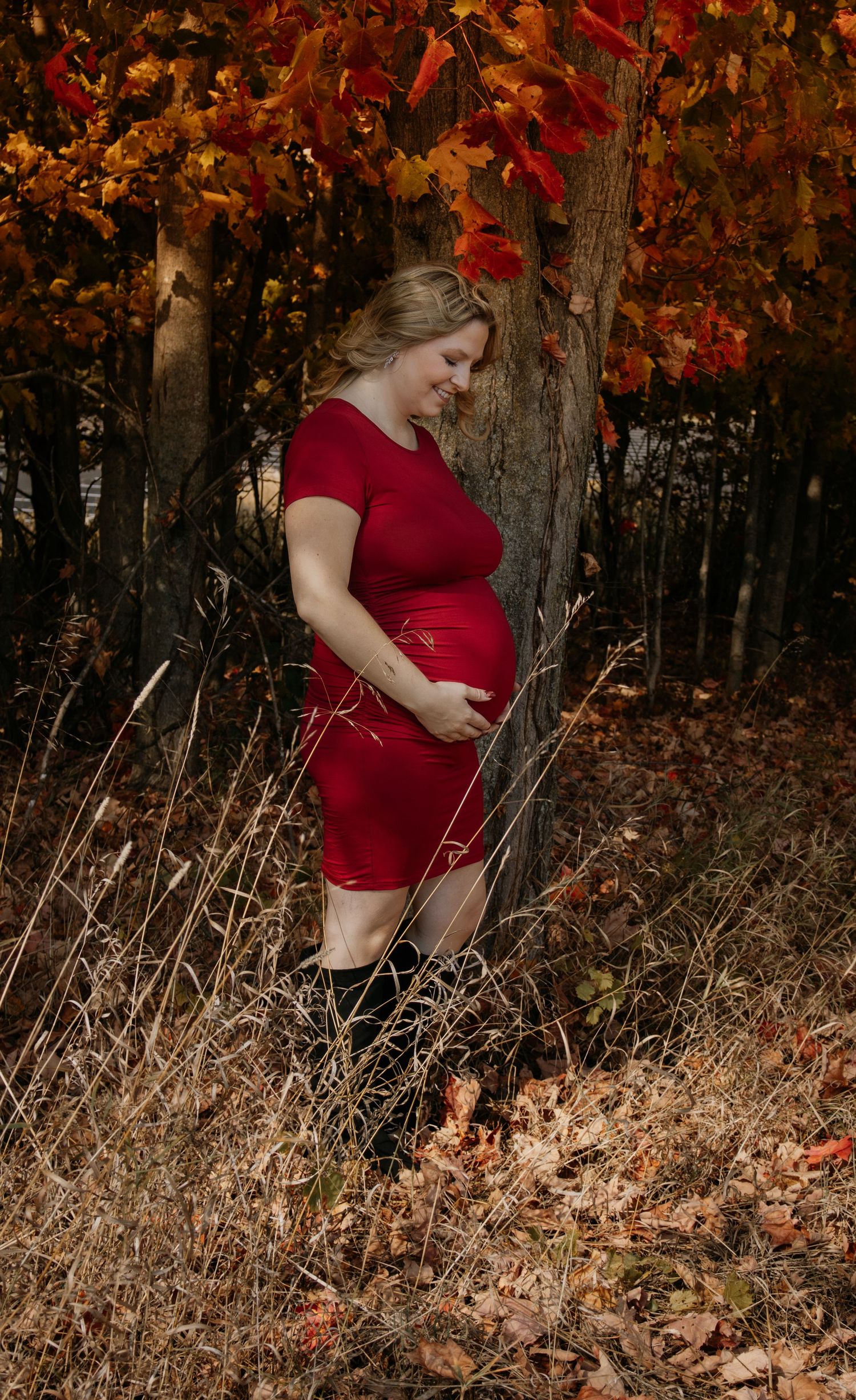 Maternity photography in a wooded area with rich autumn colors and fallen leaves.