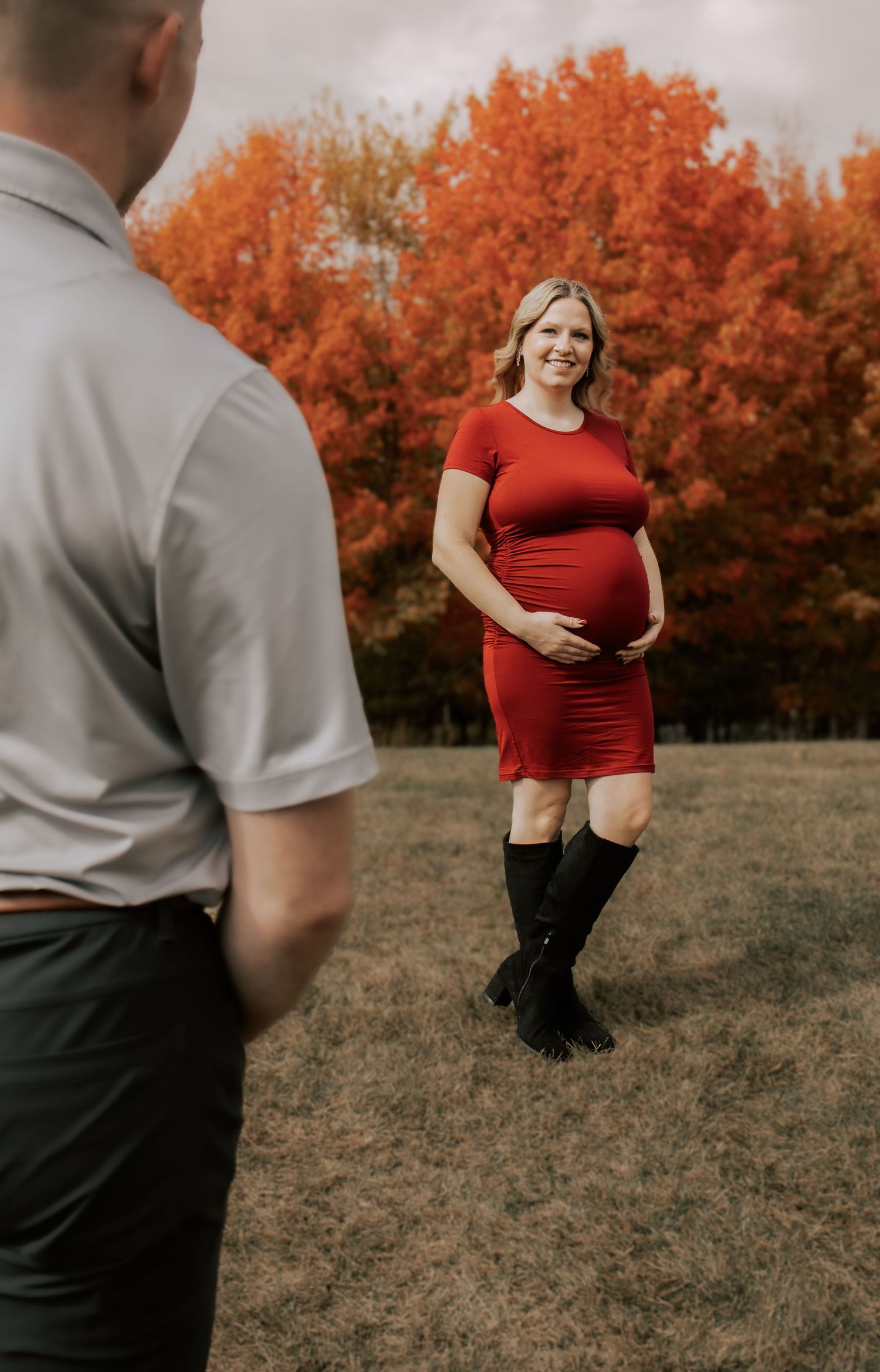 Autumn maternity photoshoot outdoors with vibrant orange foliage in the background.