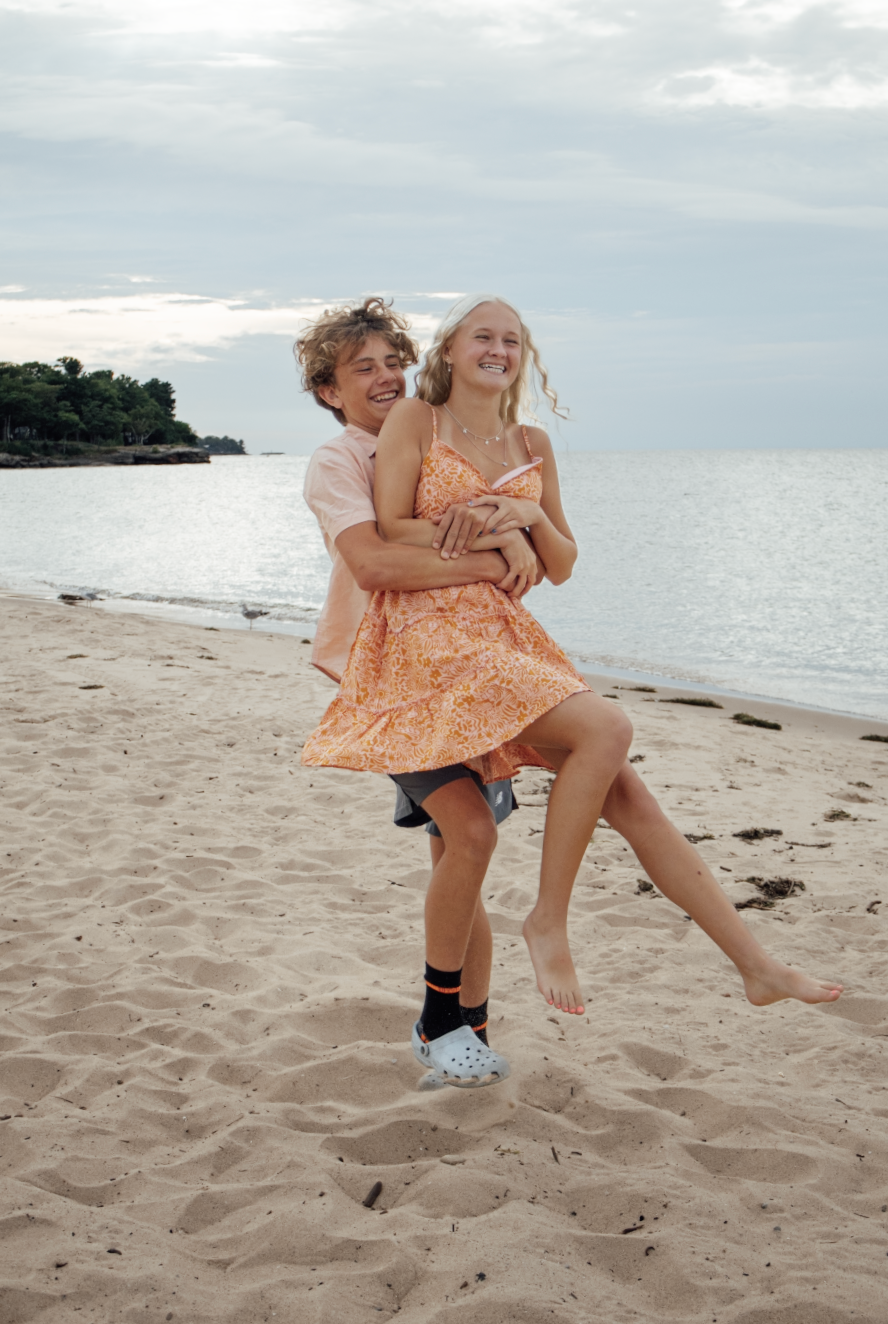 People share joyful interactions on a beach with ocean views and sandy landscape at sunset.