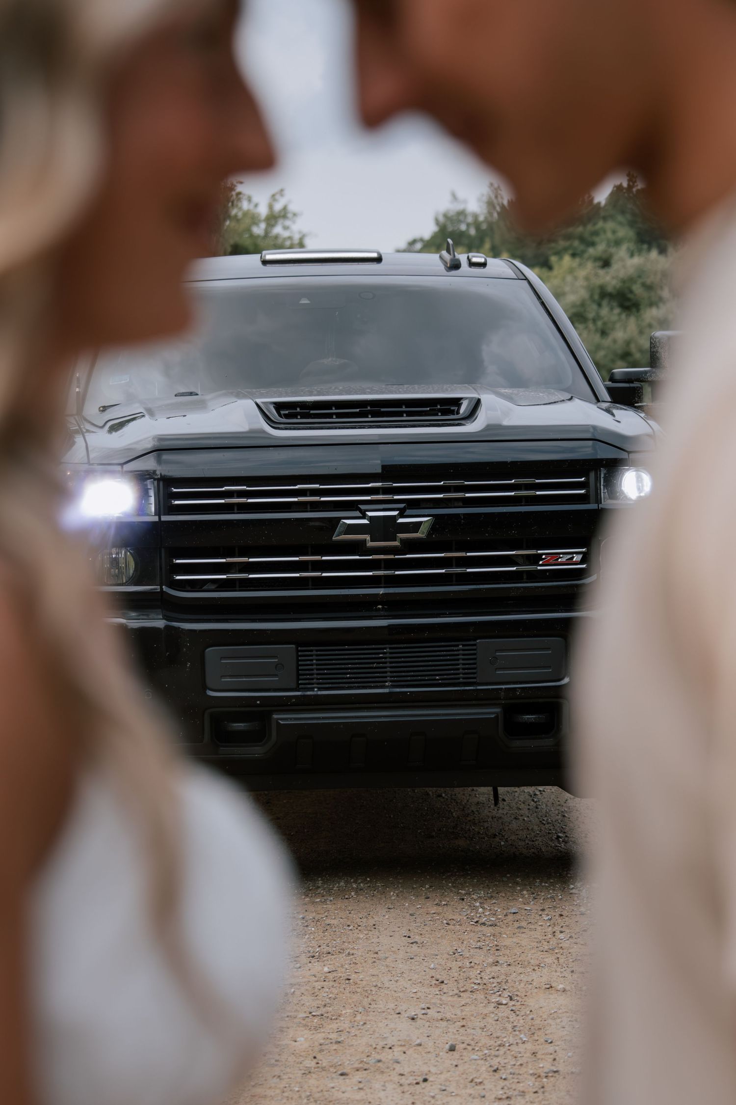 A black Chevrolet Z71 truck with headlights on, framed by a blurred couple in the foreground on a gravel path.