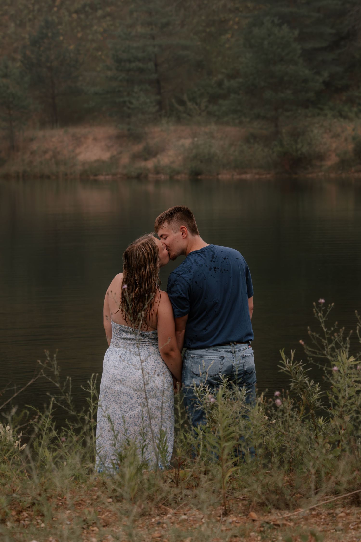 Couple sharing a romantic moment by a serene lake, surrounded by lush greenery, in a tender embrace.