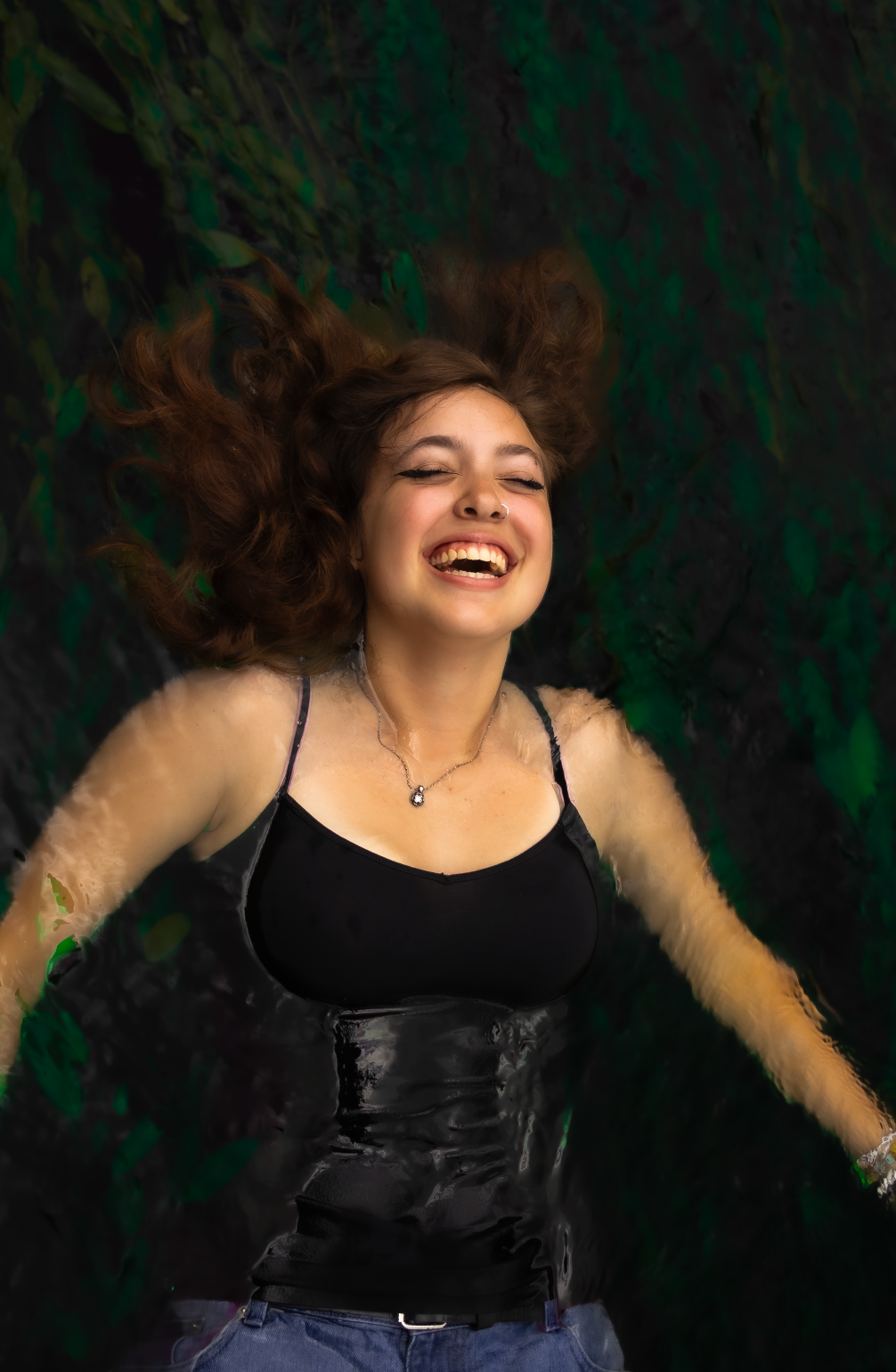 A joyful expression captured against a dark green background while wearing a black corset top and pendant necklace.