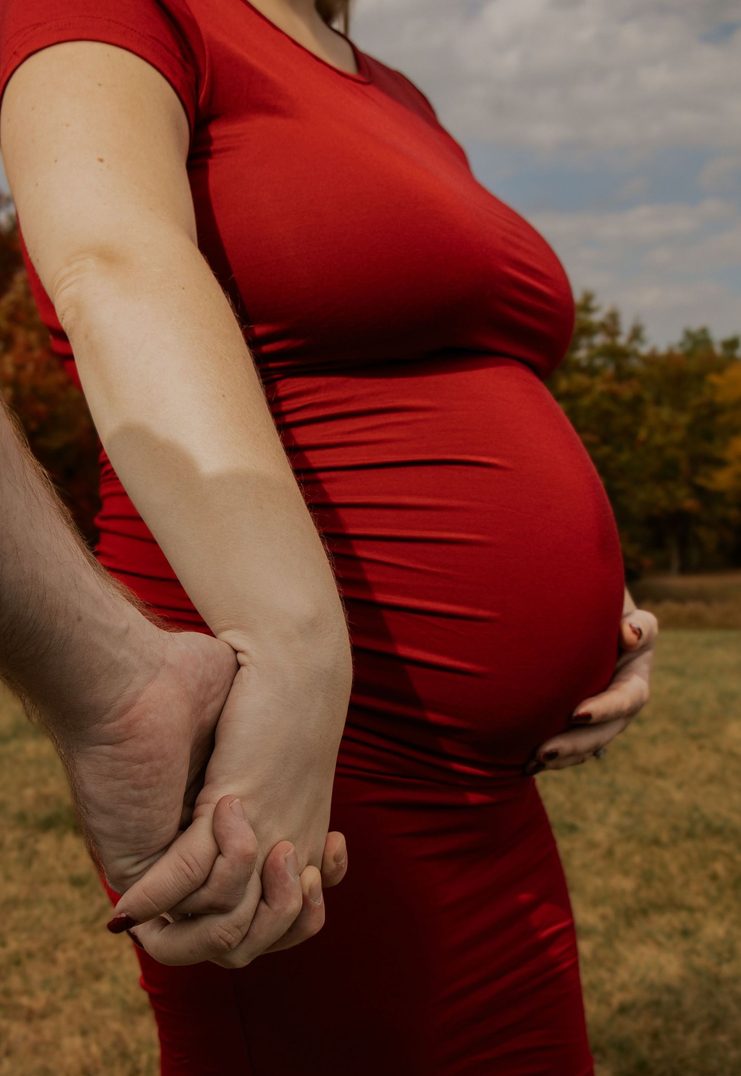Close up shots of a red maternity dress showing a growing baby bump against an autumn backdrop.