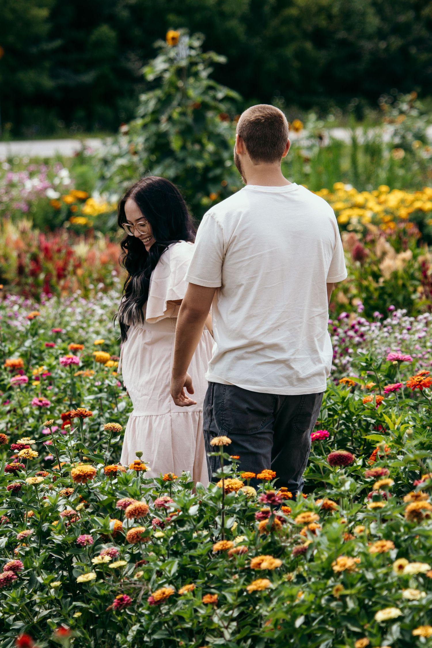 Couple holding hands walking through a vibrant colorful flower field with zinnias in bloom.