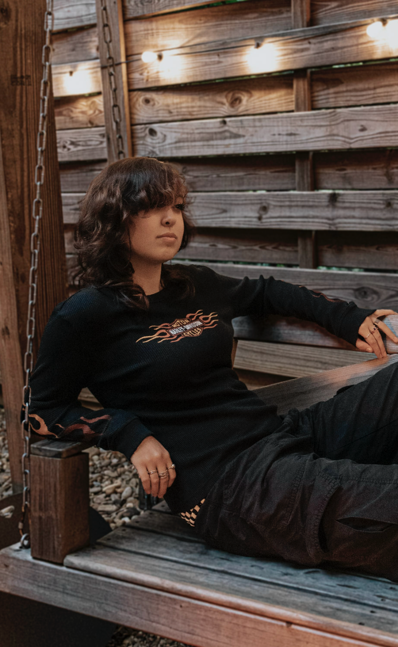 Someone lounges on a rustic wooden platform at dusk, illuminated by warm string lights overhead.