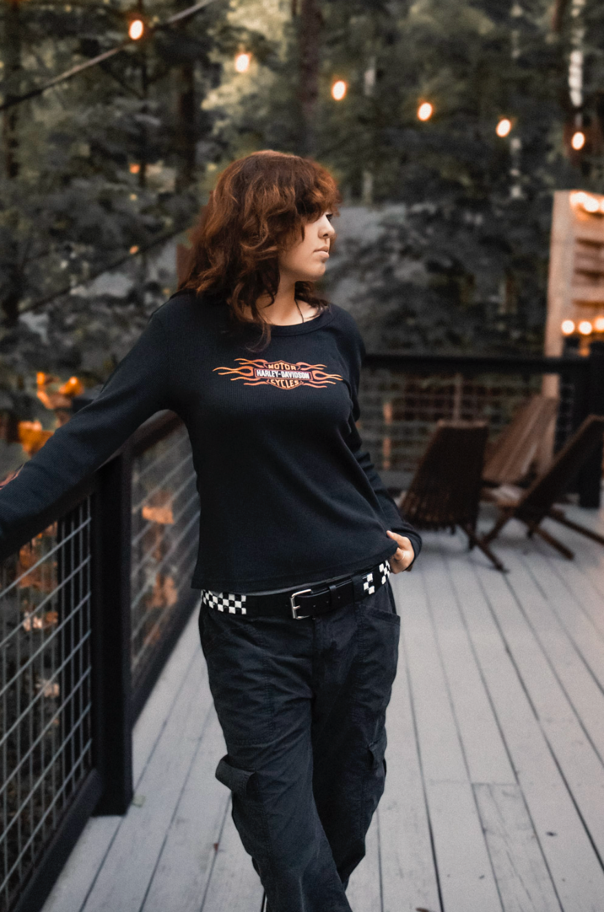 A person in dark clothing walks across an outdoor wooden deck with string lights overhead in the evening.