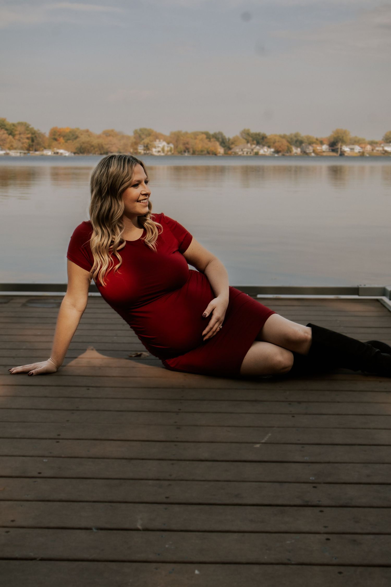 Artistic maternity poses captured on a lakeside dock during an autumn photoshoot.