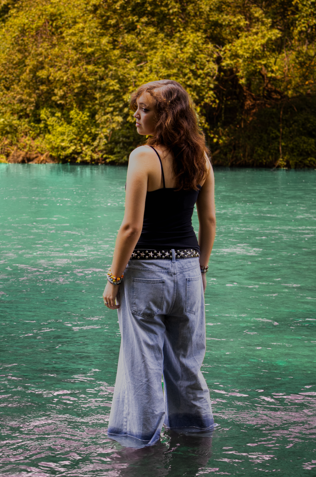 Someone standing in turquoise water wearing jeans and a black tank top, with golden autumn foliage in background.
