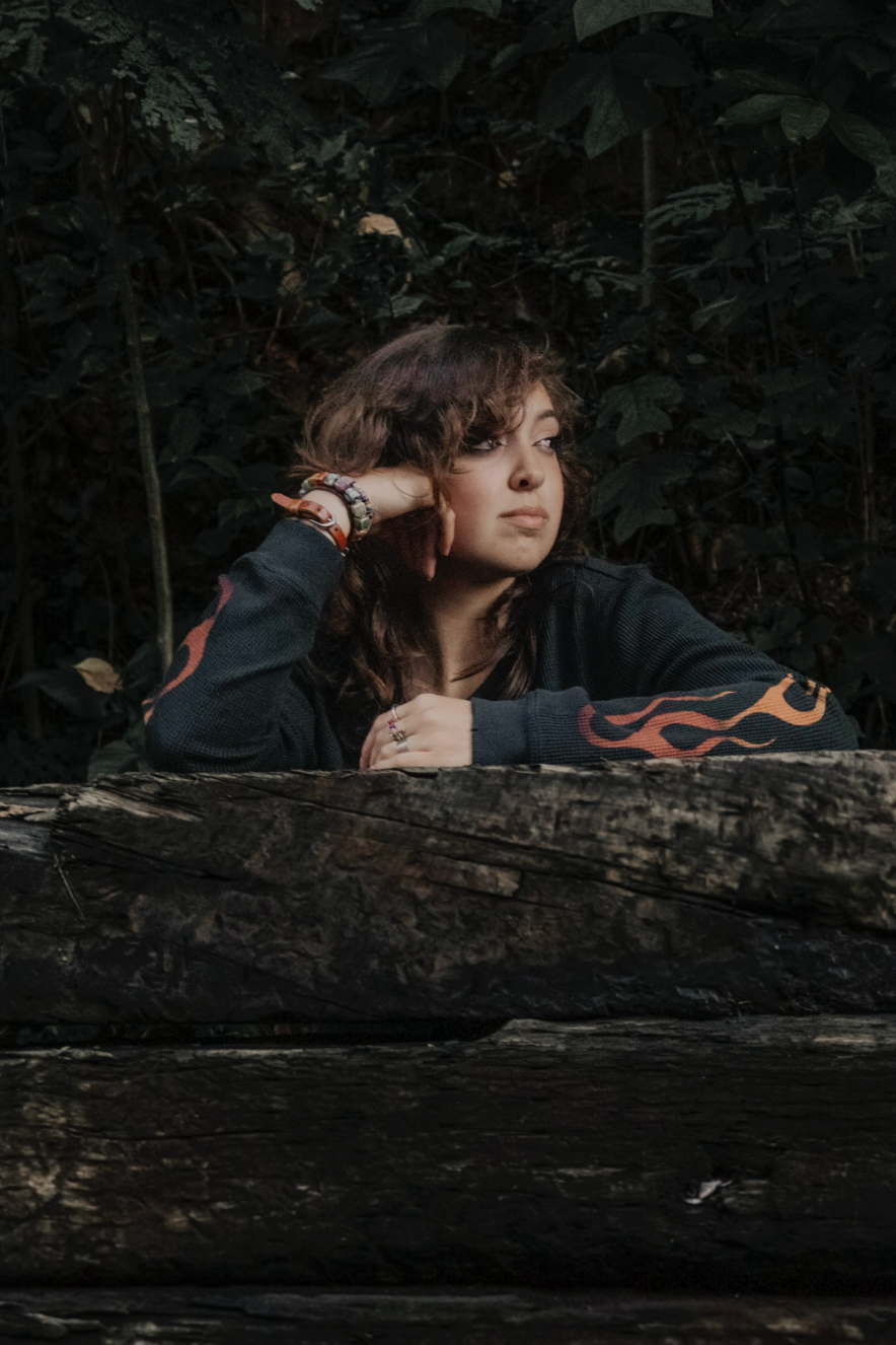 Moody artistic portrait behind a dark log in a shadowy forest setting.