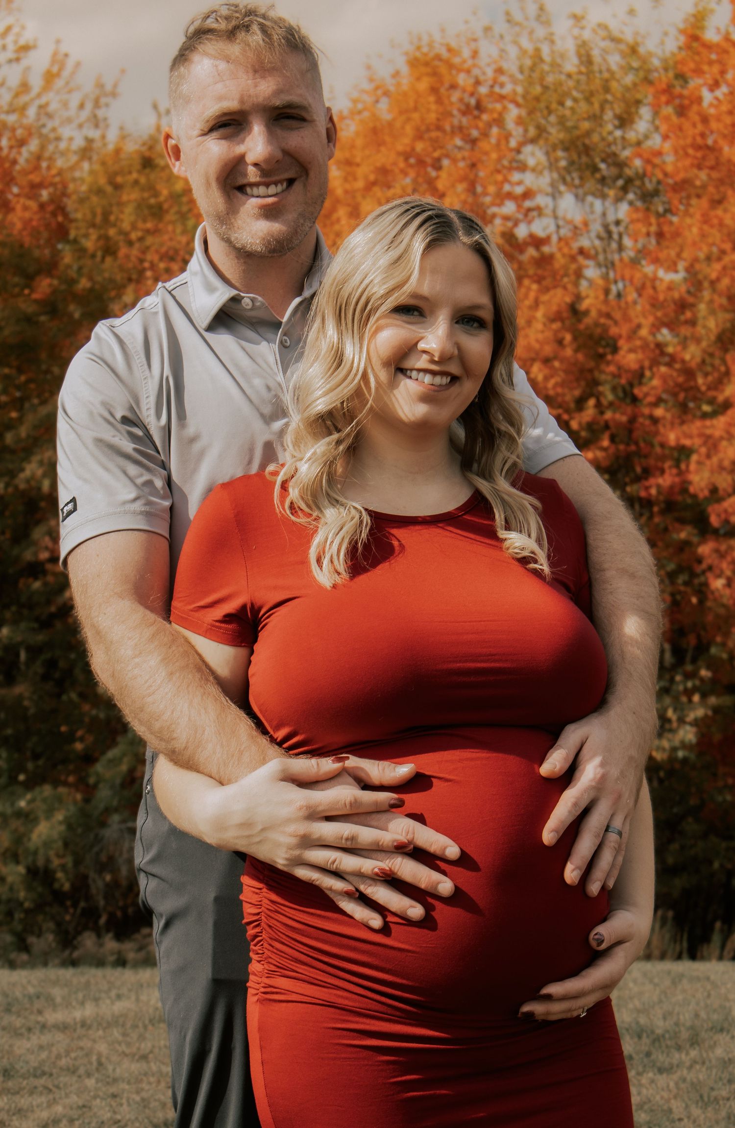 A tender maternity moment captured outdoors with fall colors in the background.