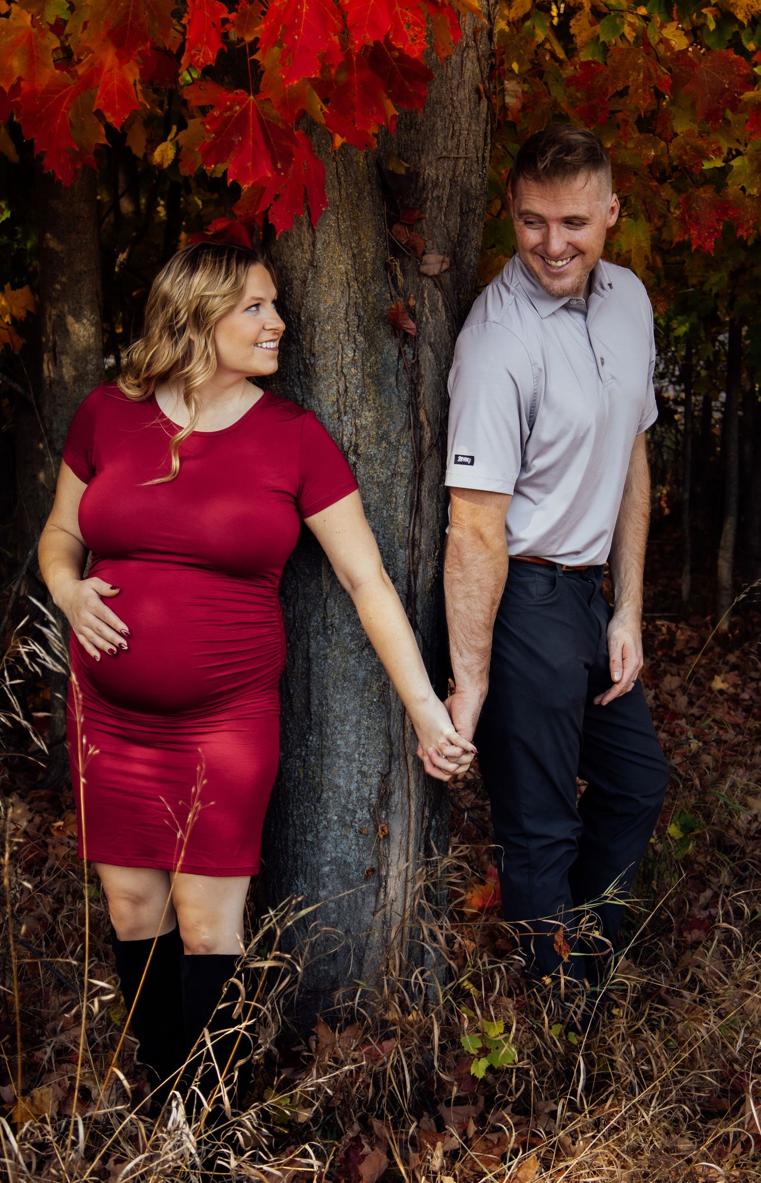 Fall maternity photos with bright red maple leaves and rustic woodland backdrop.