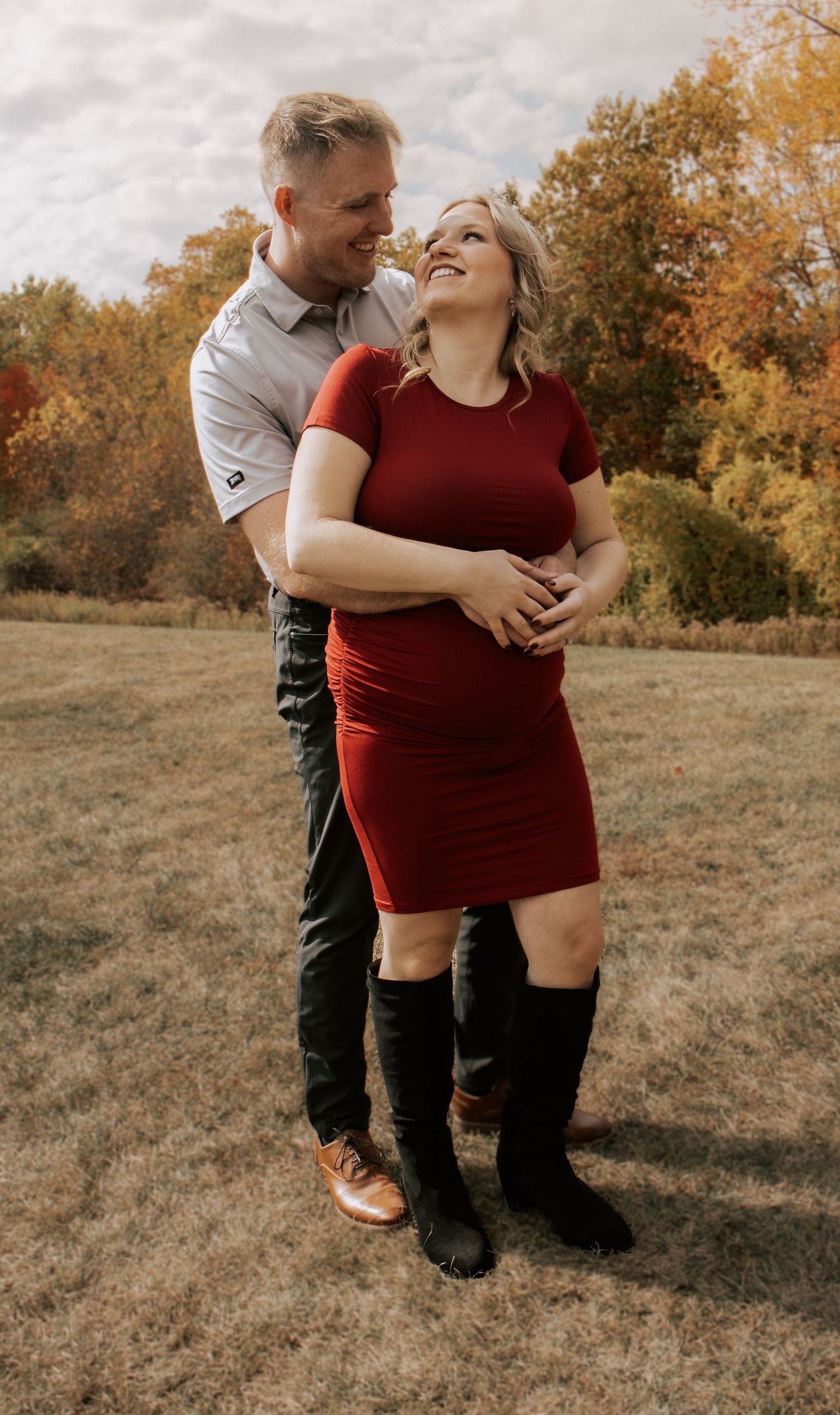A loving couple embraces in a field surrounded by fall foliage.