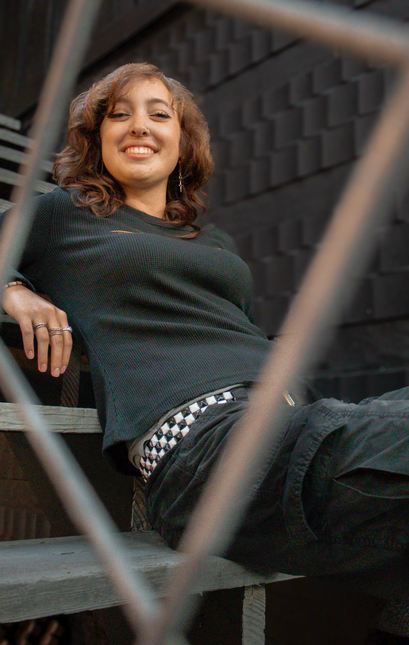 A person lounges on an industrial structure wearing a black outfit with checkered details.