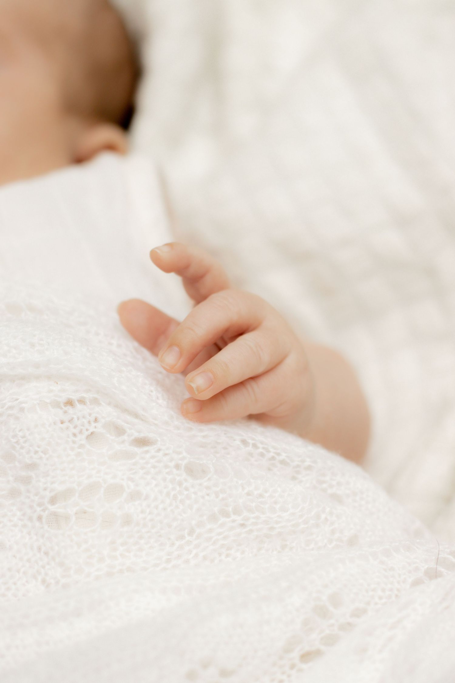 Close-up of a sleeping newborn baby's tiny hand resting on a white lace blanket.