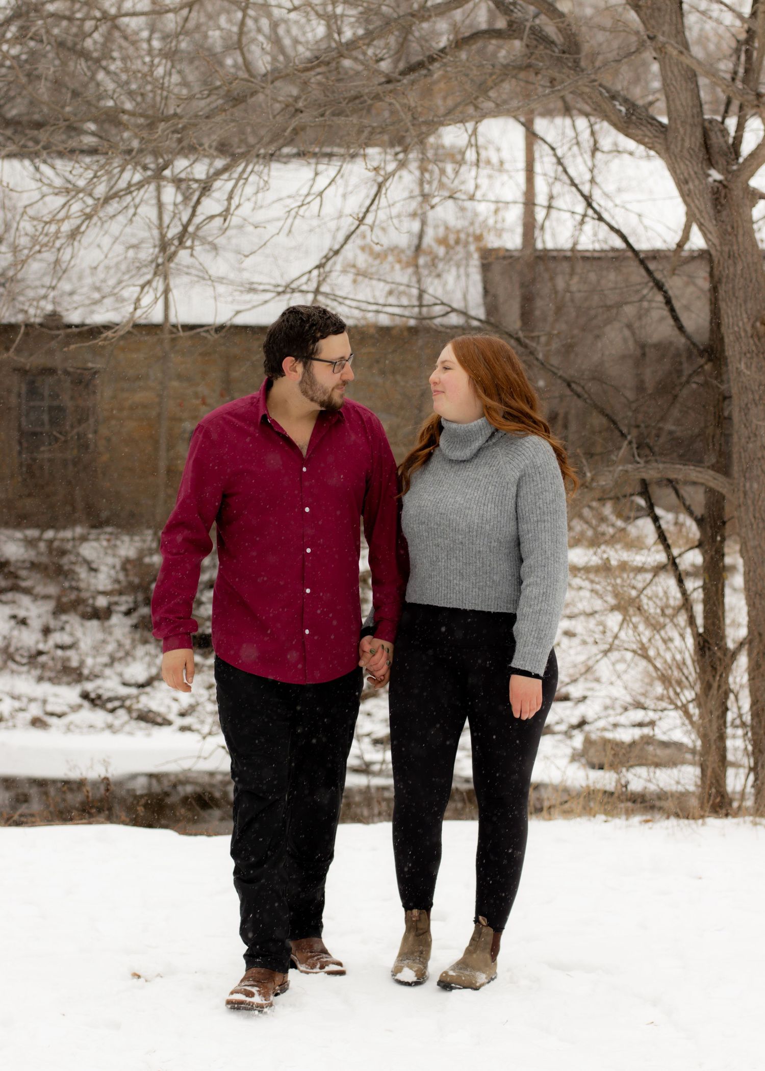 Couple holding hands and gazing at each other while walking in snowy winter landscape.