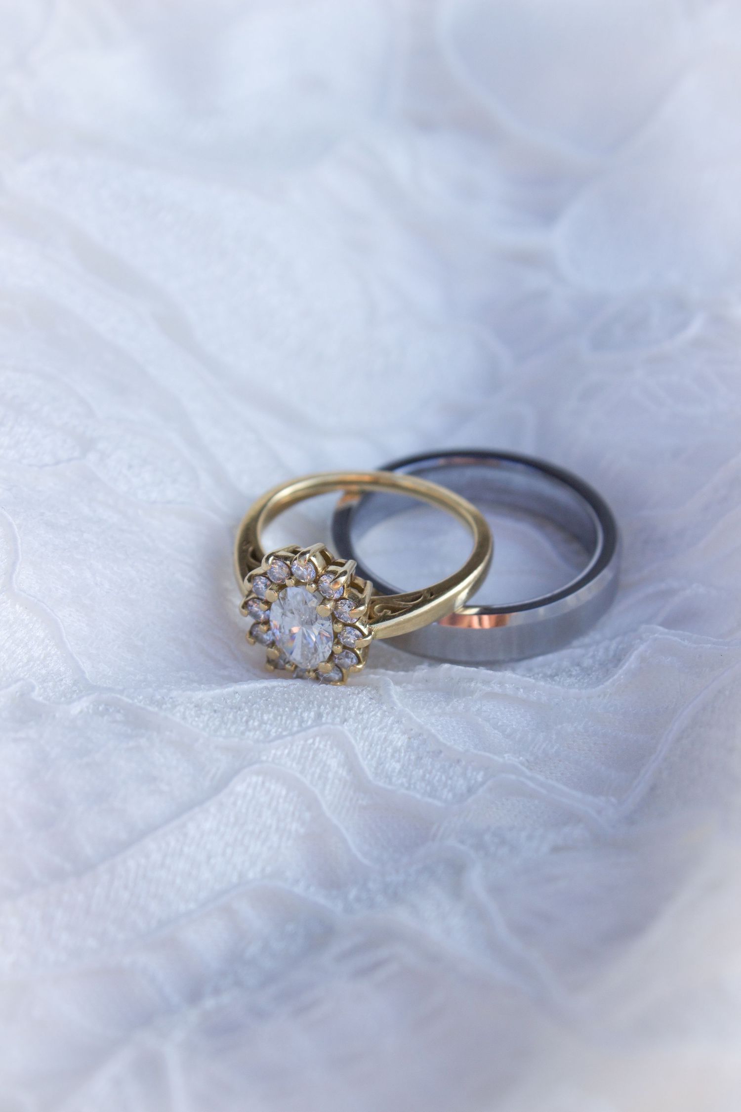Two gold and silver wedding rings with diamond halo setting displayed on white tulle fabric.