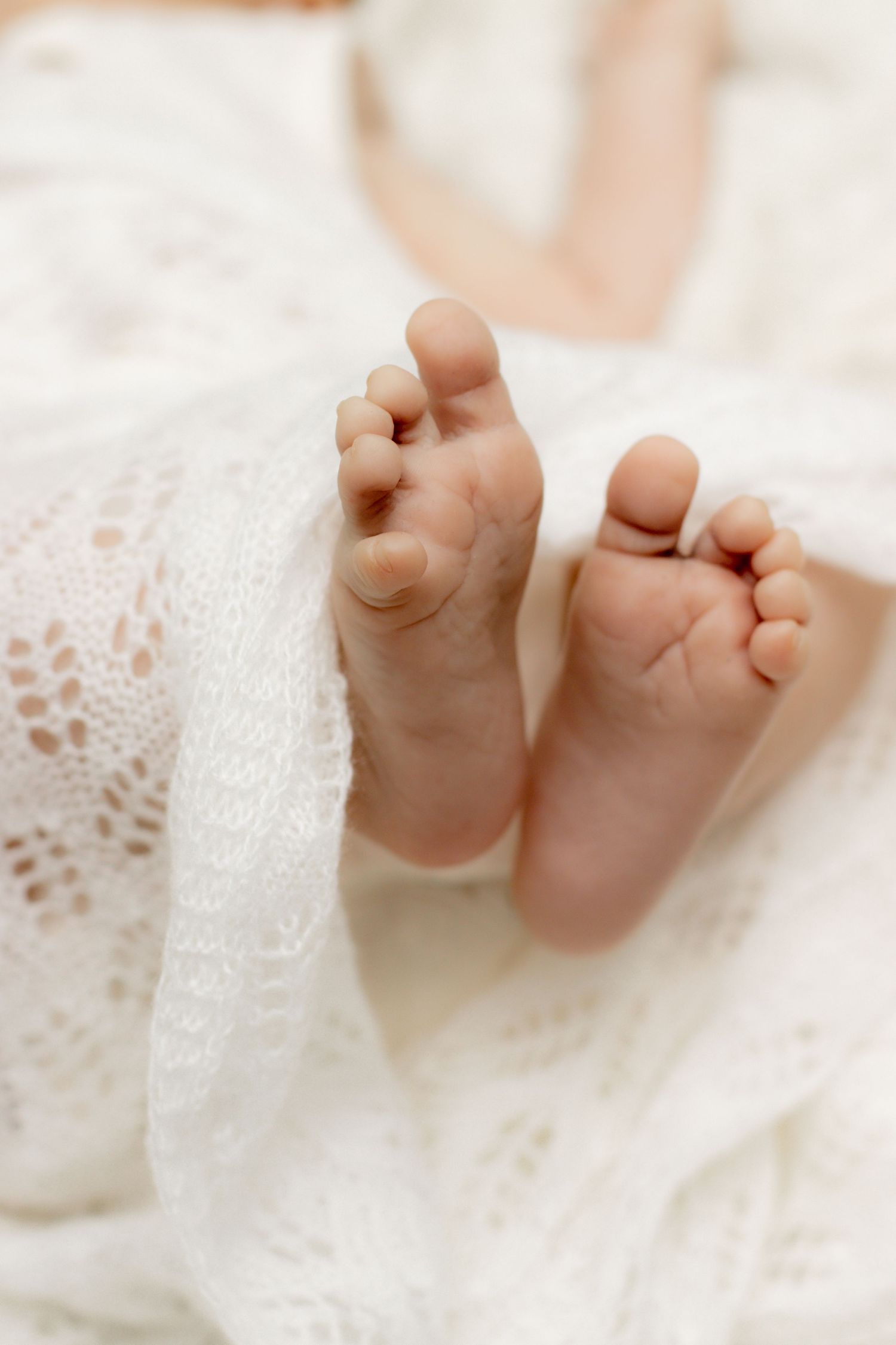 Tiny newborn baby feet peeking out from a delicate white lace blanket.
