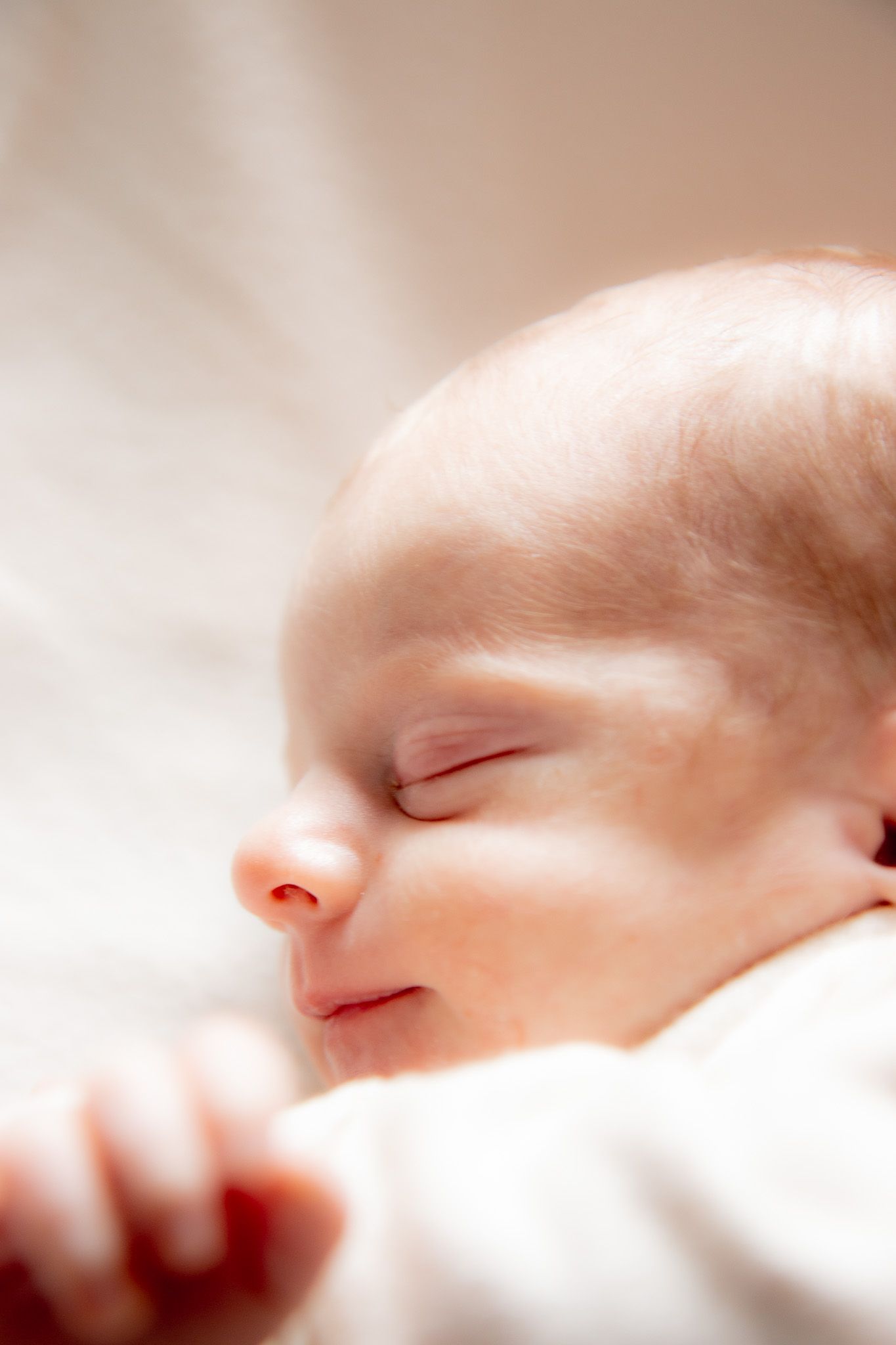 A peaceful newborn baby sleeping soundly, with tiny clenched fist visible against a soft white background.