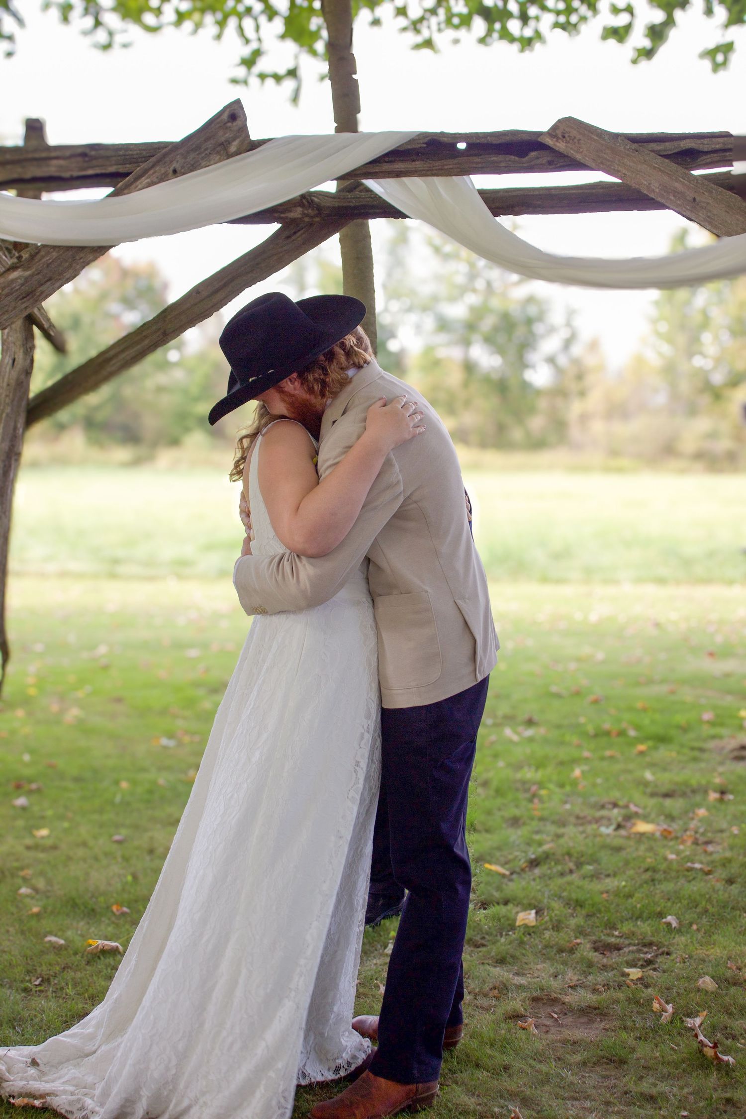 Bride and groom share first kiss under rustic wooden arch at outdoor wedding.