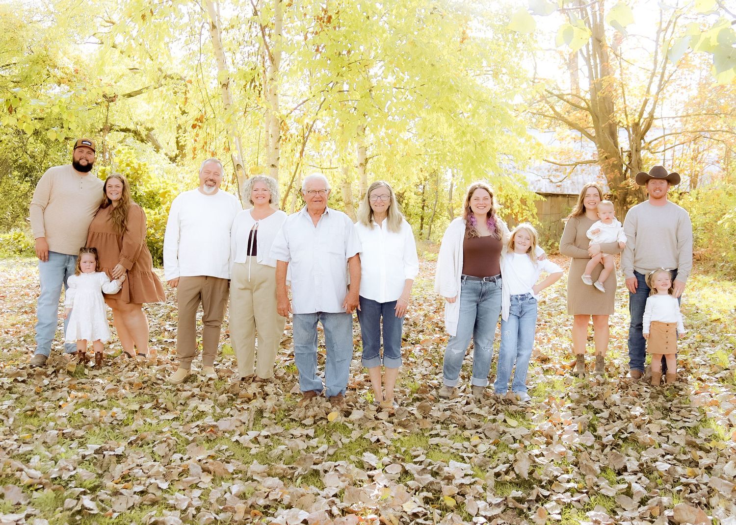 Extended multigenerational family of ten poses among fallen autumn leaves with golden trees in background.