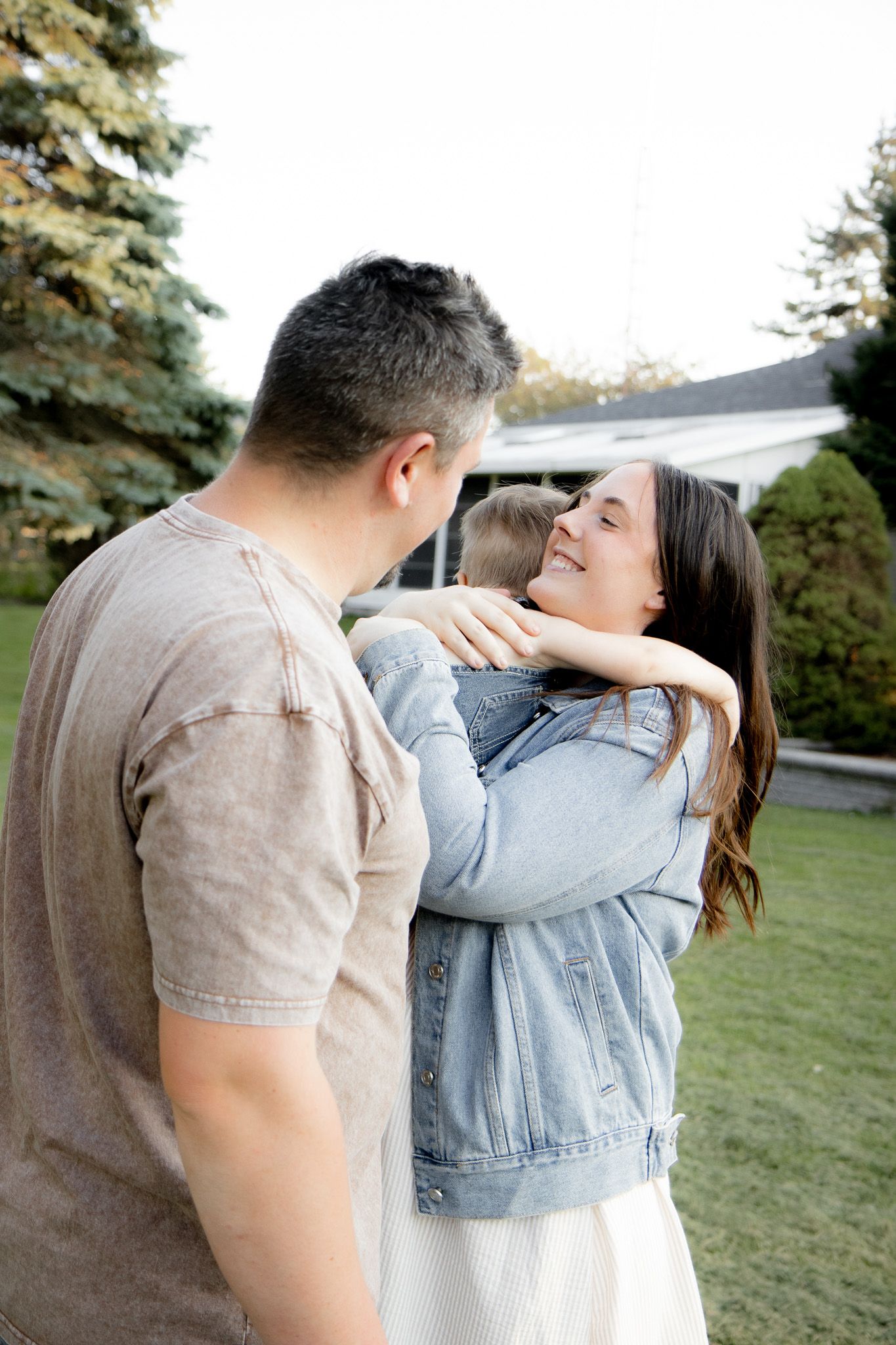 A happy family shares a warm embrace outdoors in front of their home on a sunny day.