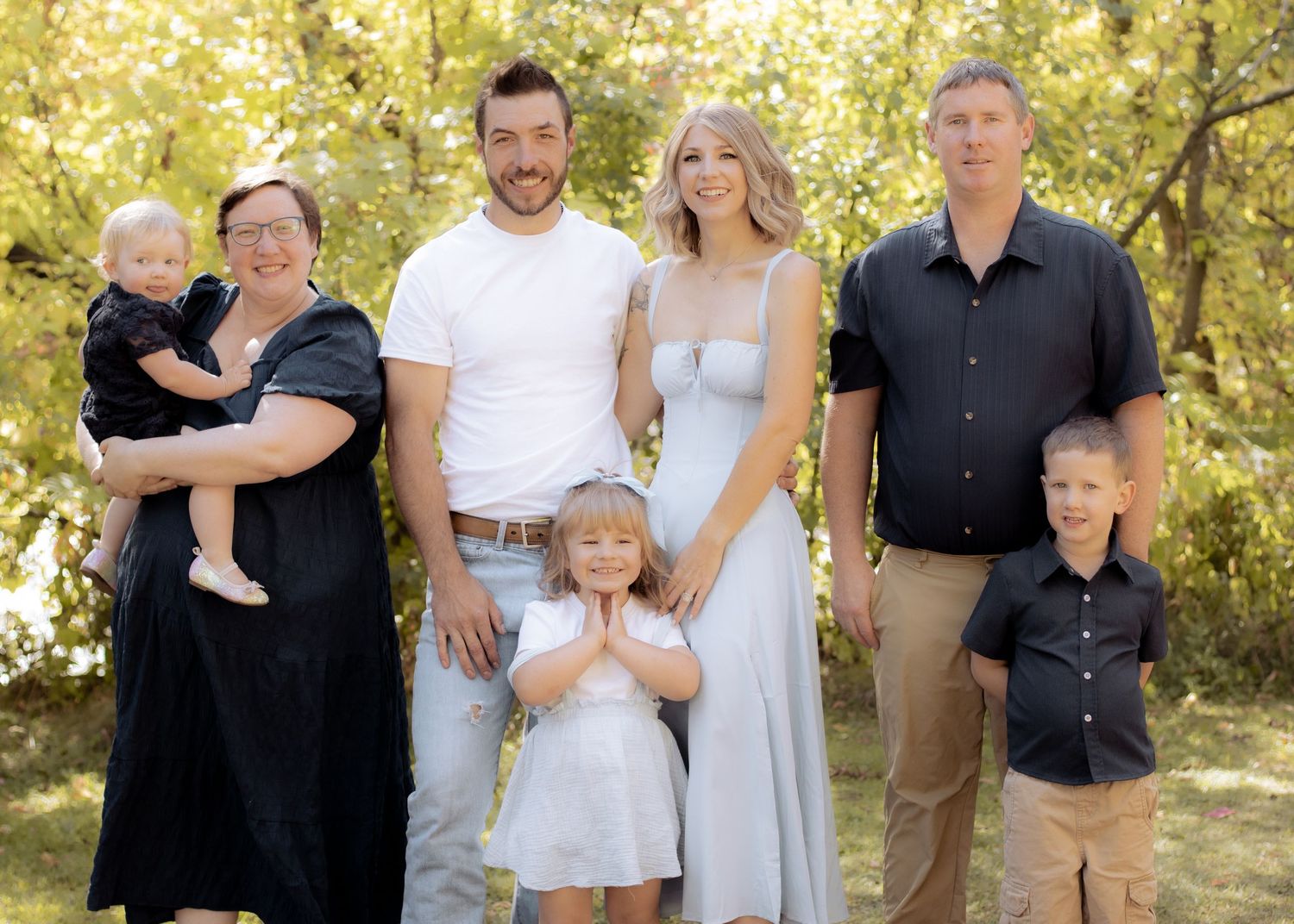 Extended family of seven posing together outdoors with golden trees, including young children.